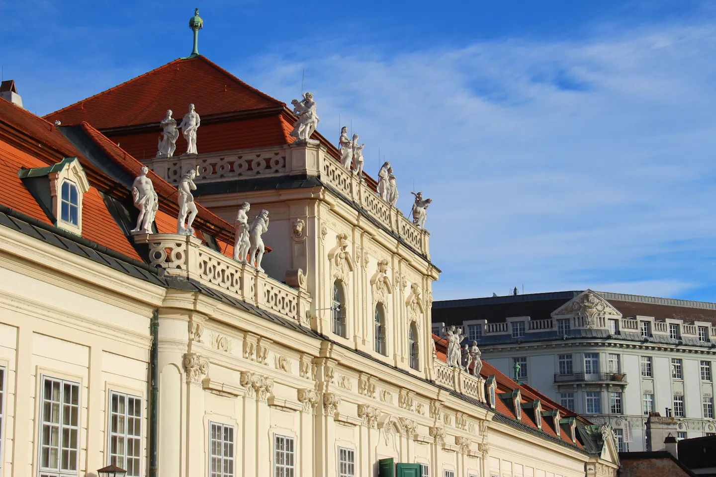 Carved statues along the roofline of the Belvedere palace in Vienna against a clear blue sky