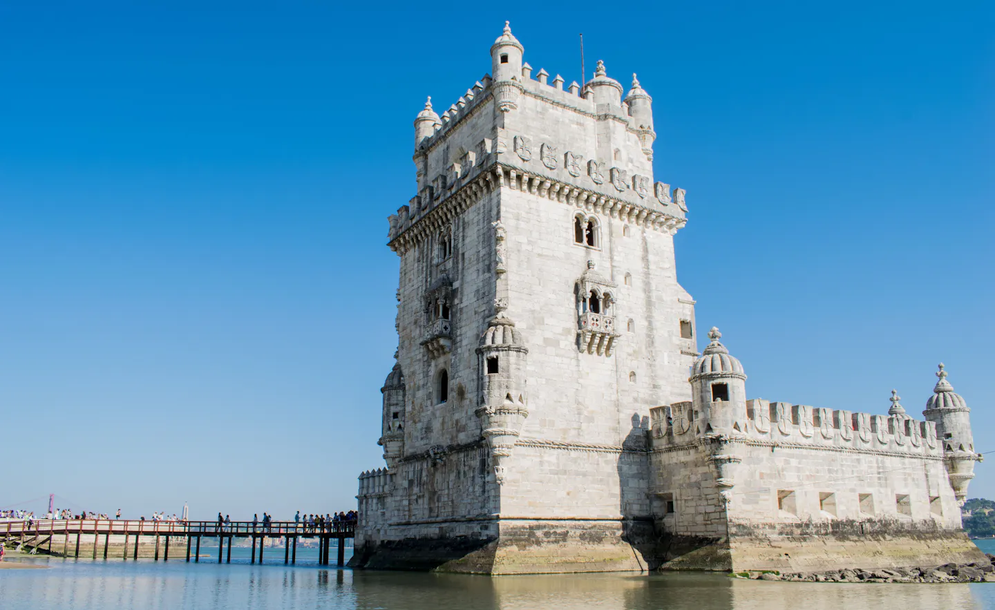 The white stone Belém Tower standing in the Tagus river in Lisbon against a deep blue sky
