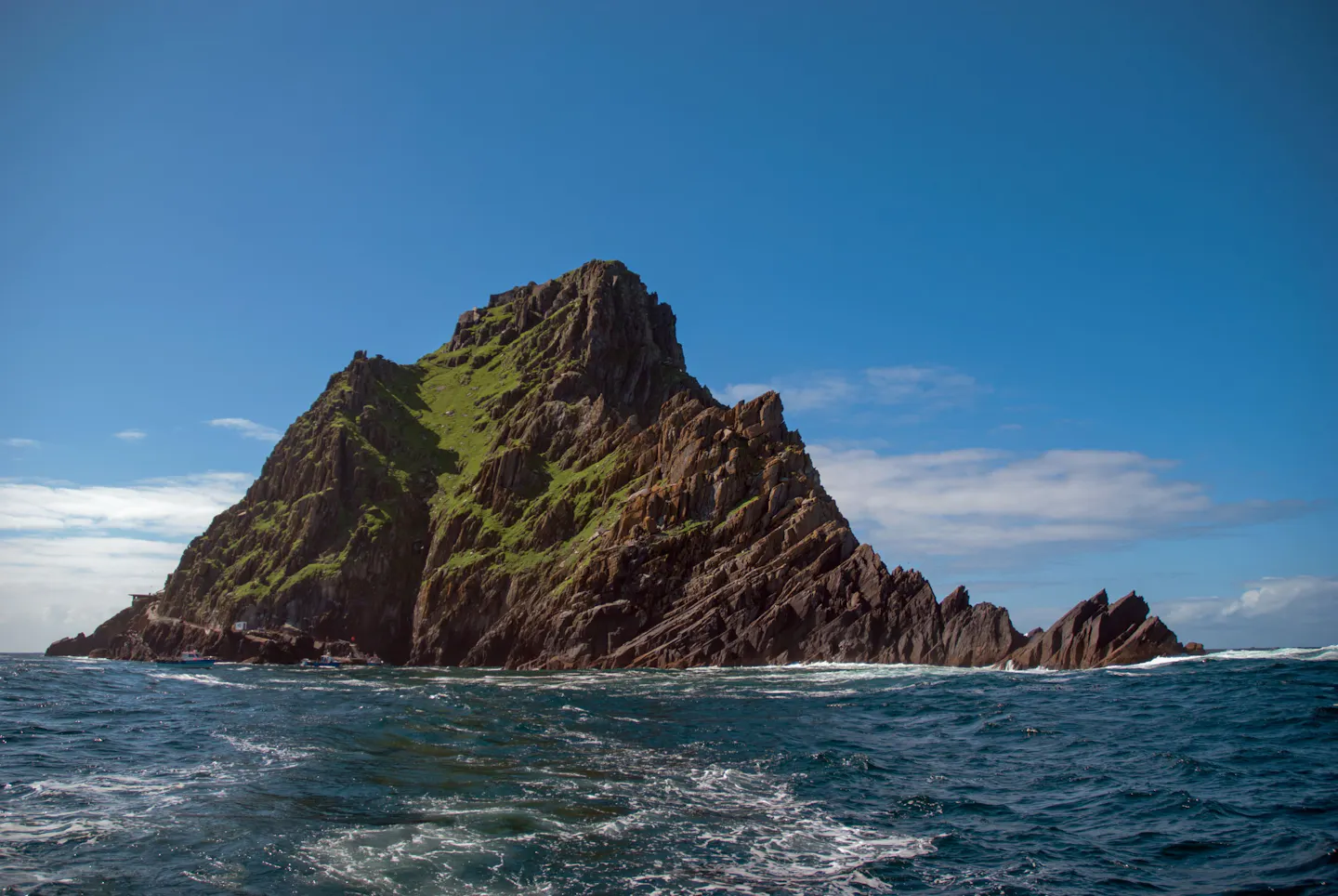 The steep green-and-grey pyramid of Skellig Michael rising from the dark Atlantic off the Kerry coast under a blue sky