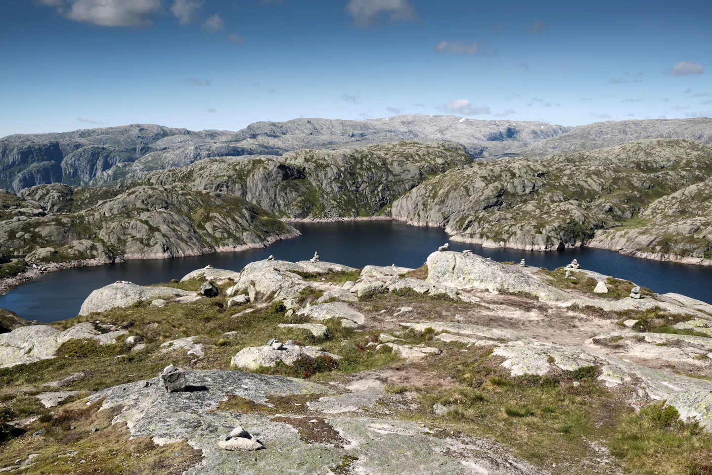 A dark lake set among bare rock and moss on a high Norwegian mountain plateau under a blue sky