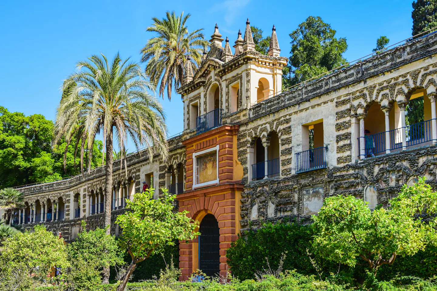 Sunlit gallery wall and orange trees in the gardens of the Real Alcazar in Seville under a clear blue sky