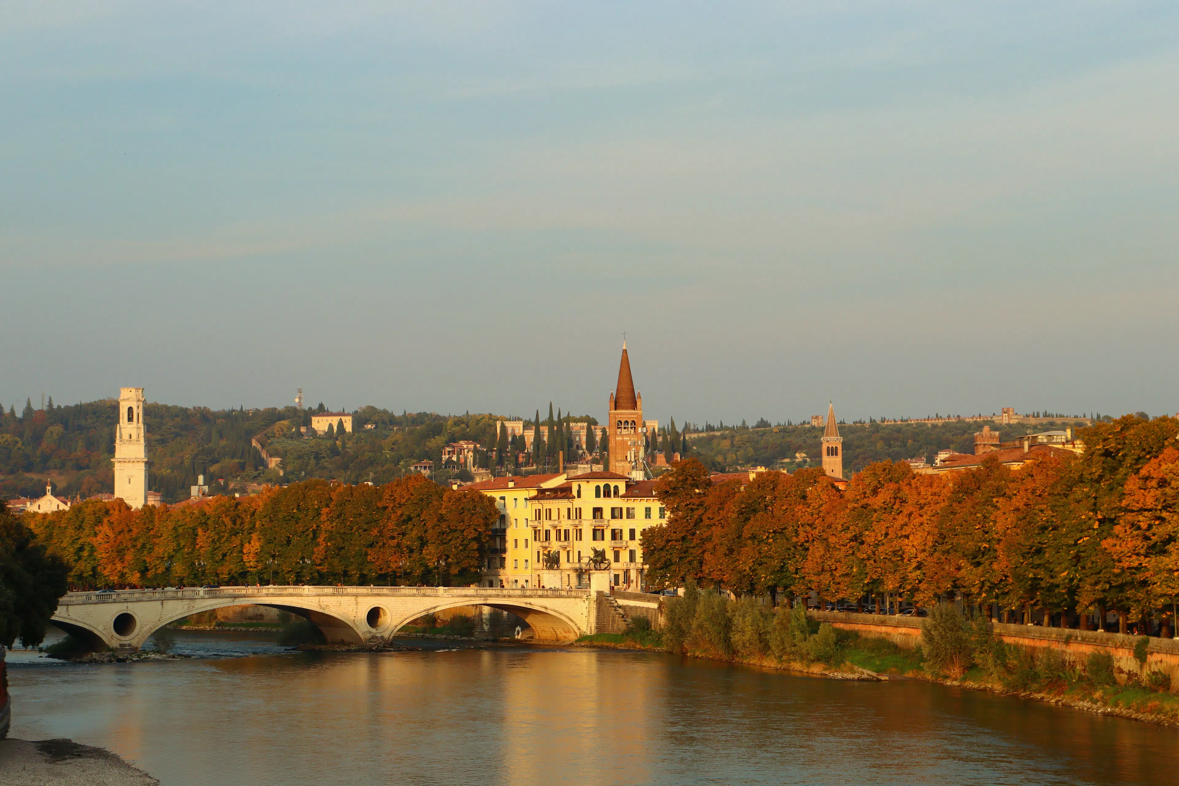 Autumn trees turning orange along the Adige in Verona with the Ponte Pietra in evening light