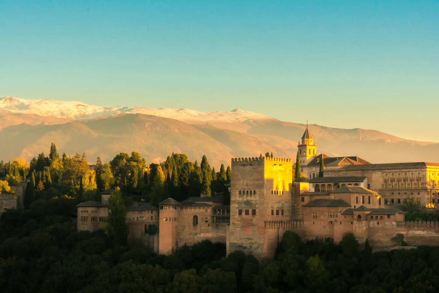 The Alhambra on its wooded ridge in Granada with the snow-capped Sierra Nevada behind