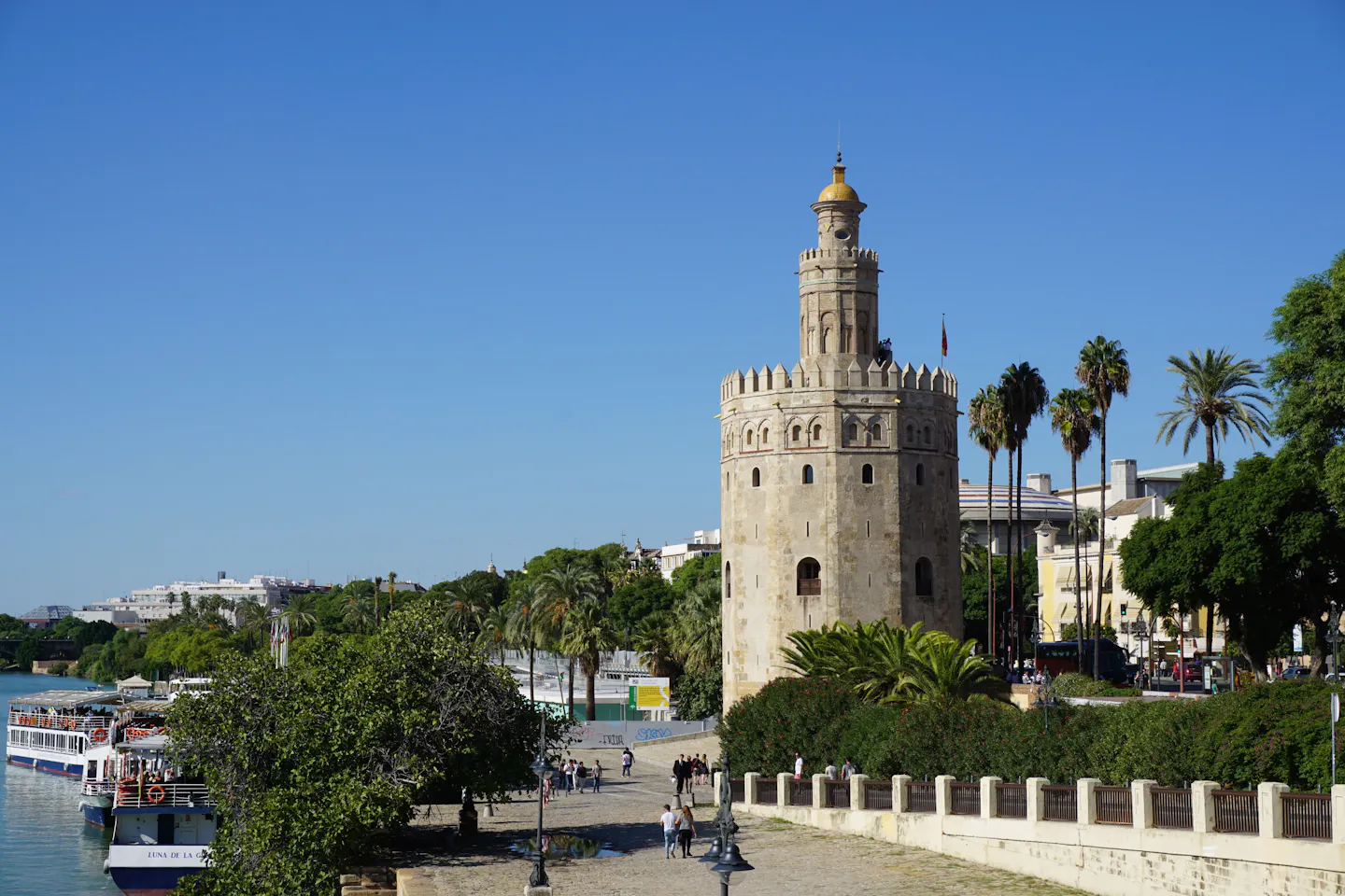 The Torre del Oro above the palm-lined bank of the Guadalquivir in Seville under a clear sky