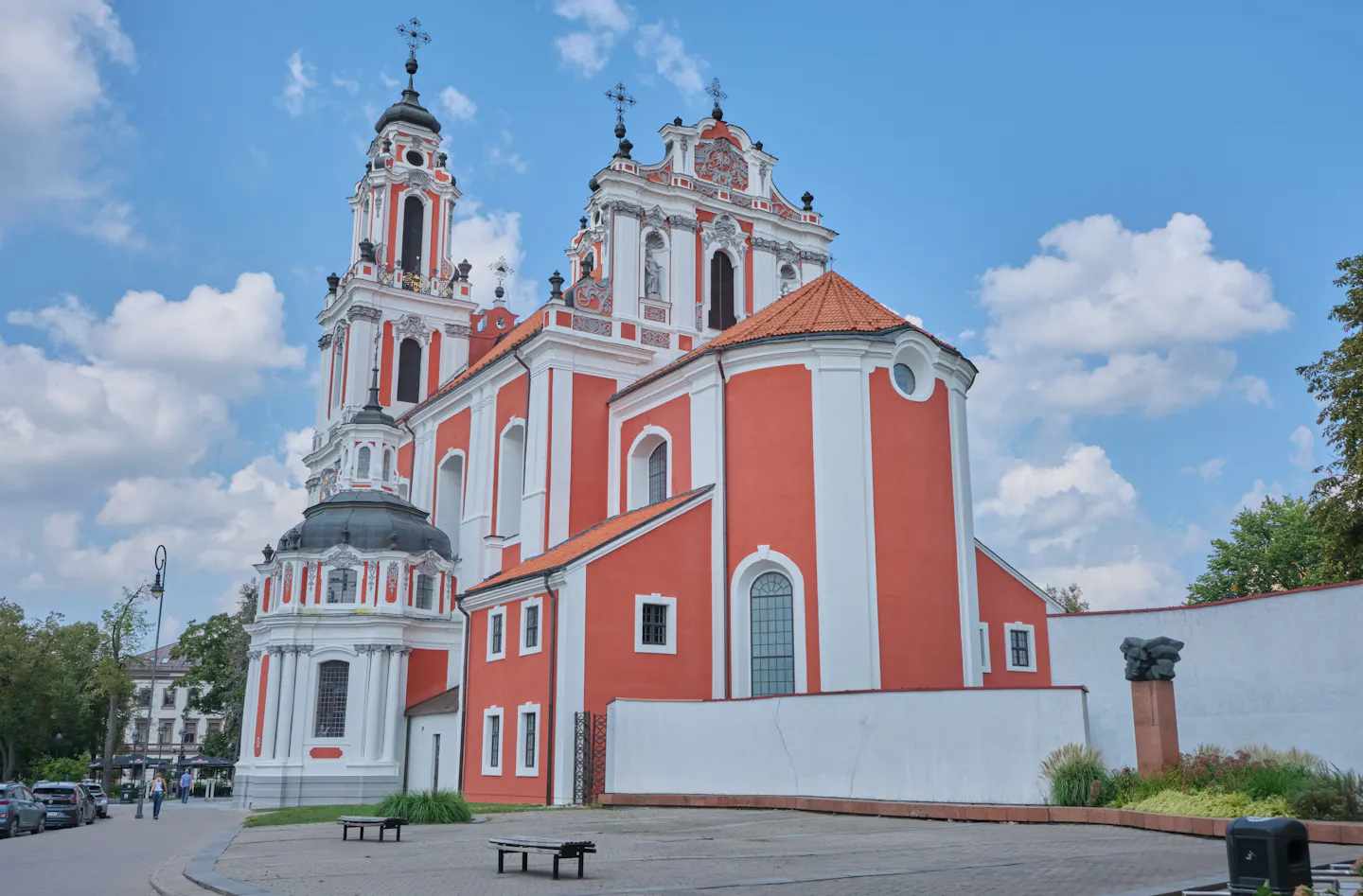The pink and white baroque facade of St Catherine's Church in Vilnius under a blue sky with white clouds