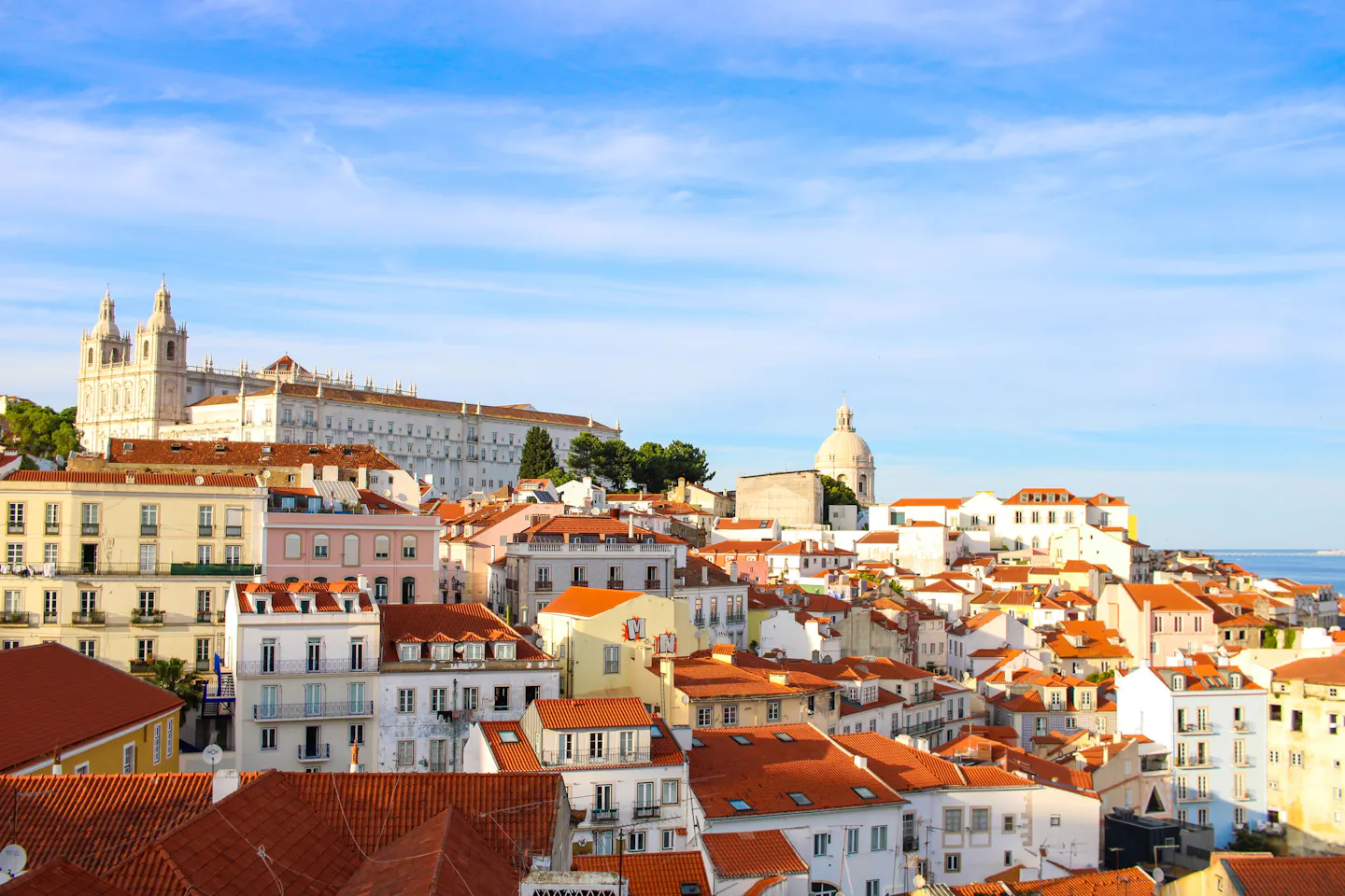 Terracotta rooftops of Lisbon's Alfama district running down towards the Tagus in afternoon light