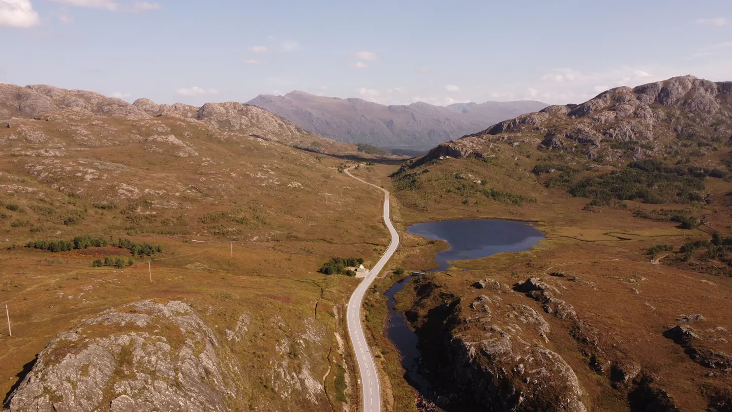 A narrow road winding through rocky Highland moorland past a small loch