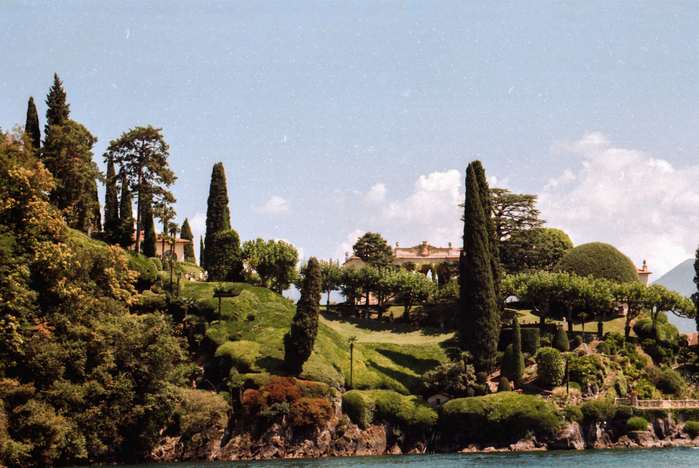 A historic villa and its terraced gardens rising above the water on Lake Como among tall cypress trees