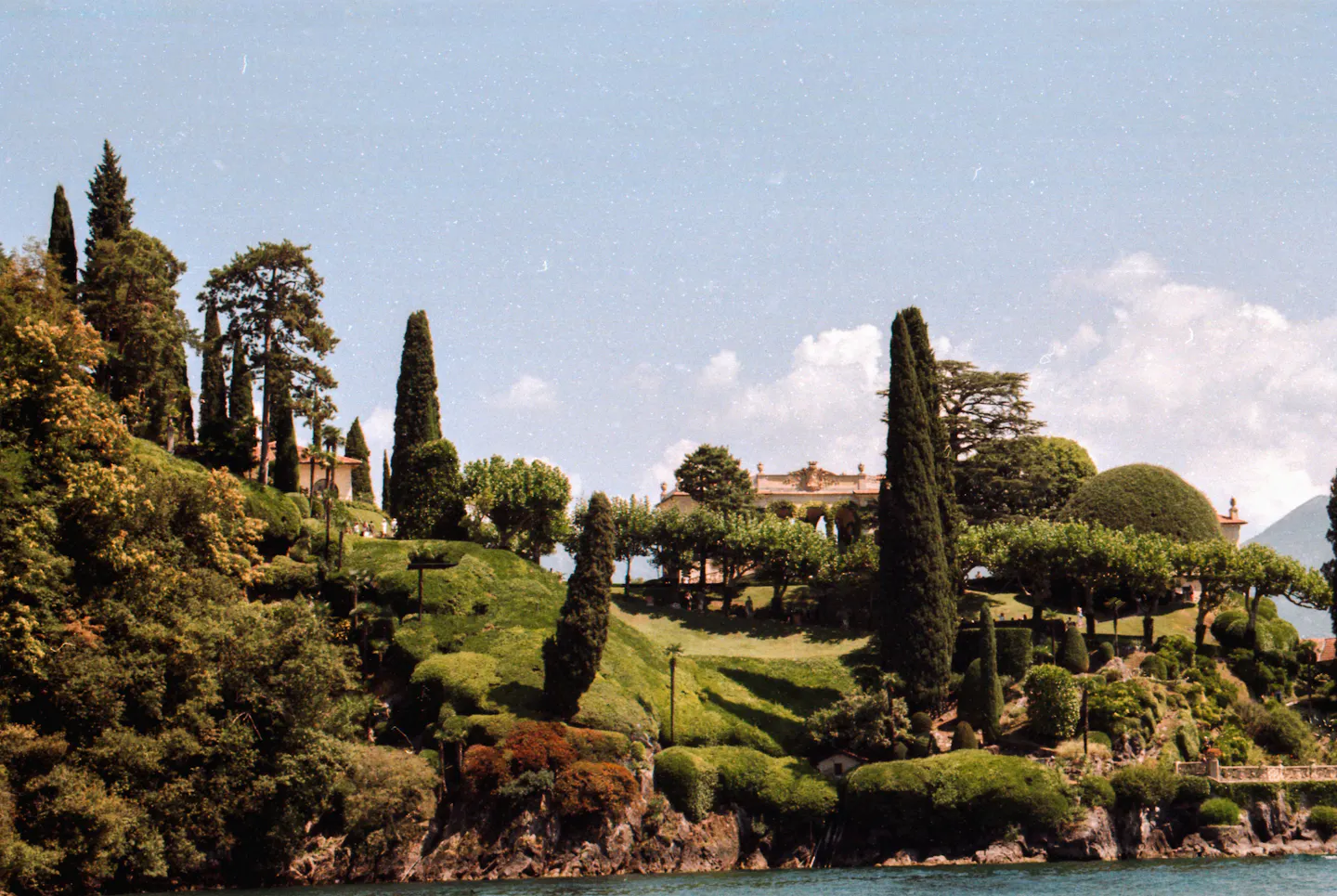 A historic villa and its terraced gardens rising above the water on Lake Como among tall cypress trees