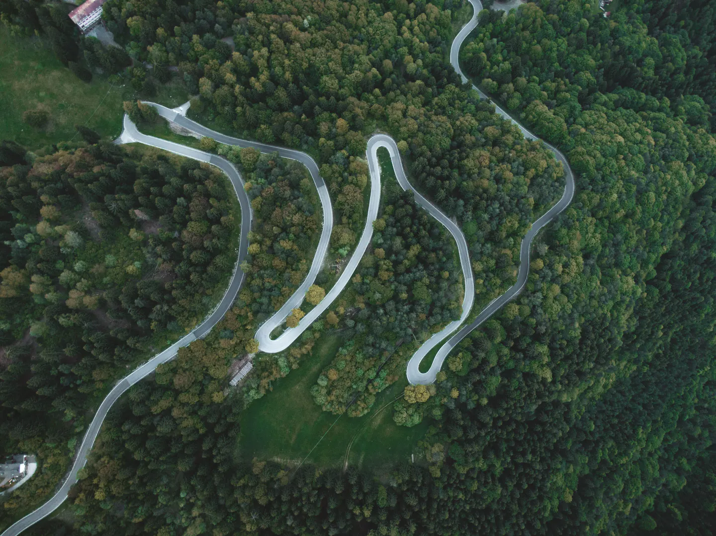 Hairpin bends of a mountain road winding down through dense green forest, seen from above