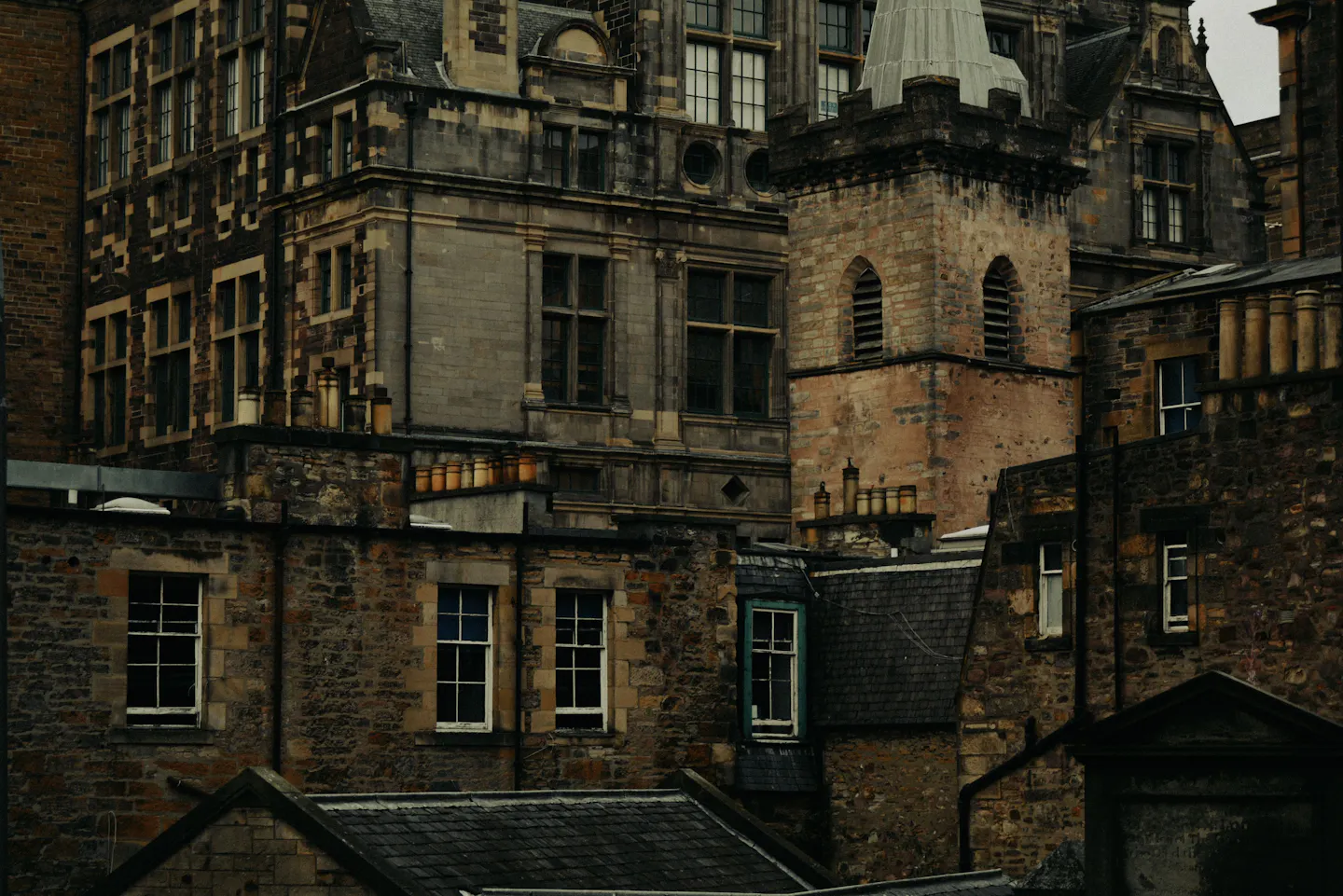 Tightly stacked Old Town stone tenements at dusk — a slate turret, ranks of clay chimney pots, sash windows and soot-darkened masonry filling the frame