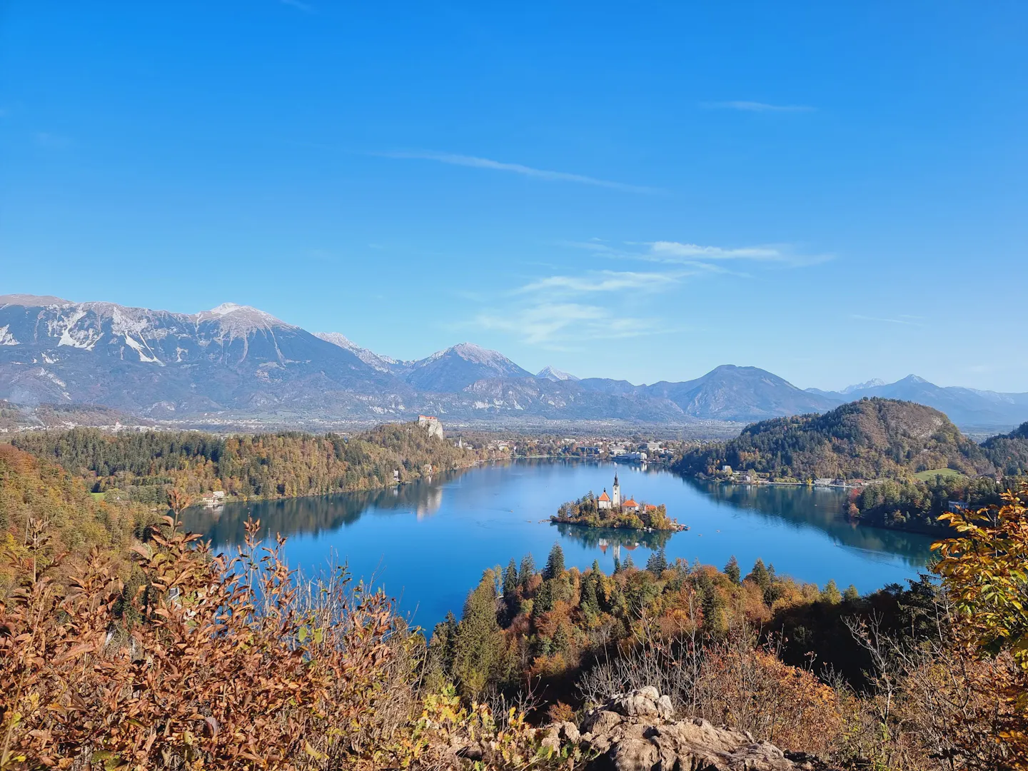 Bled Island and its church on the blue water of Lake Bled below the snow-dusted Julian Alps, framed by autumn foliage