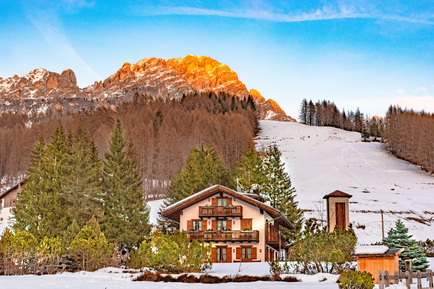 A chalet in Cortina d’Ampezzo below a Dolomite peak at sunset