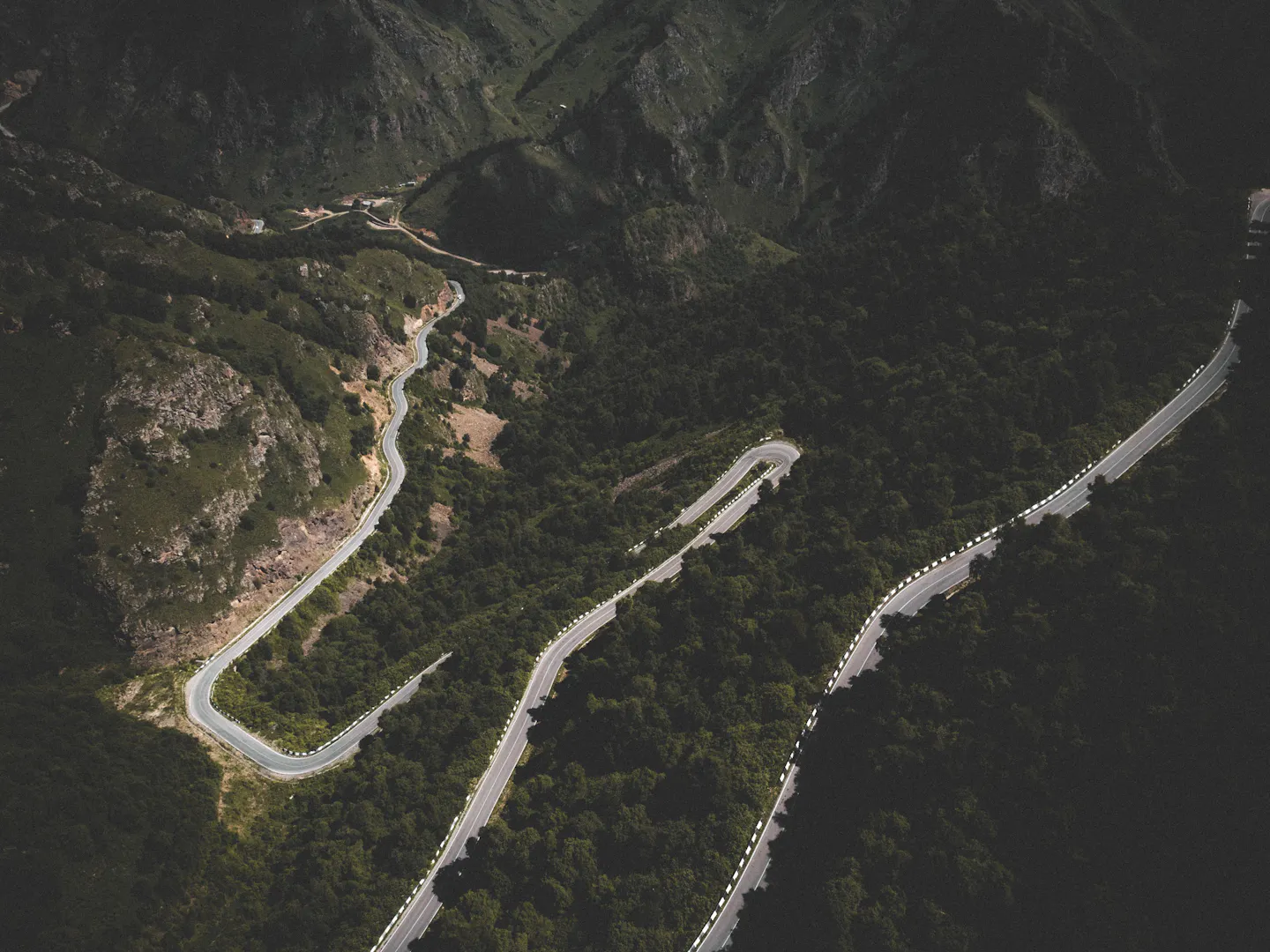 Winding mountain road curving through dense forest seen from above