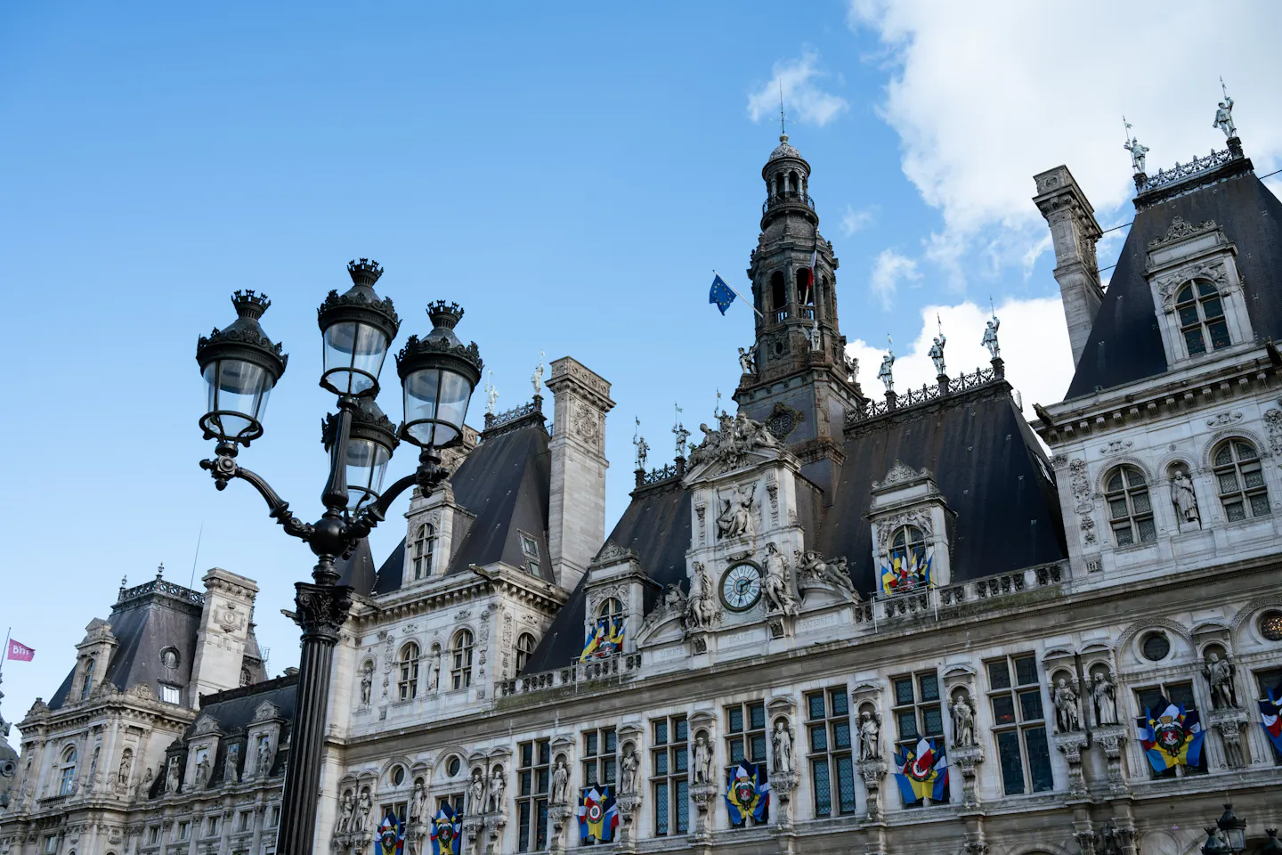The ornate facade and clock tower of the Hotel de Ville in Paris behind a cast-iron street lamp