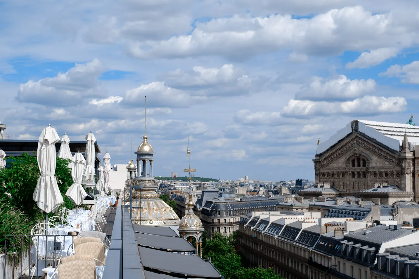 A quiet rooftop terrace with folded parasols looking out over Paris rooftops and gilded domes