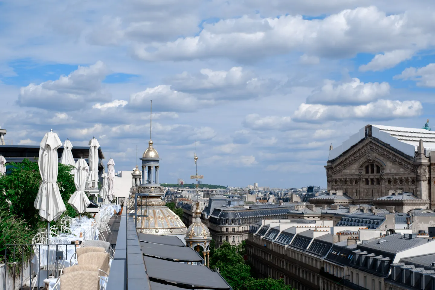 A quiet rooftop terrace with folded parasols looking out over Paris rooftops and gilded domes