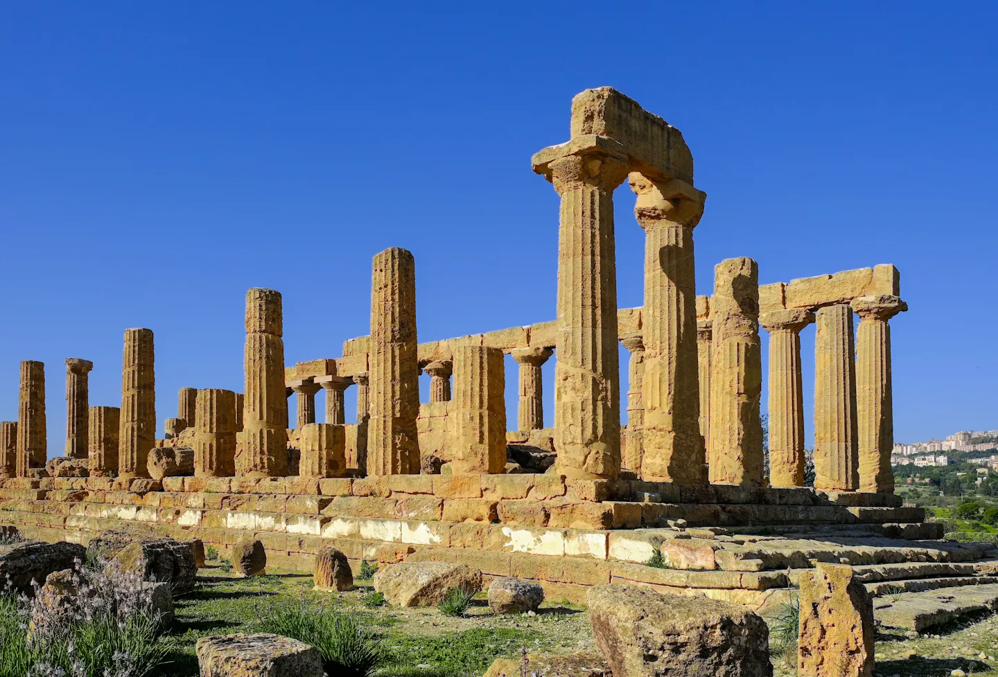 Golden Doric columns of an ancient Greek temple standing against a deep blue sky in Sicily's Valley of the Temples