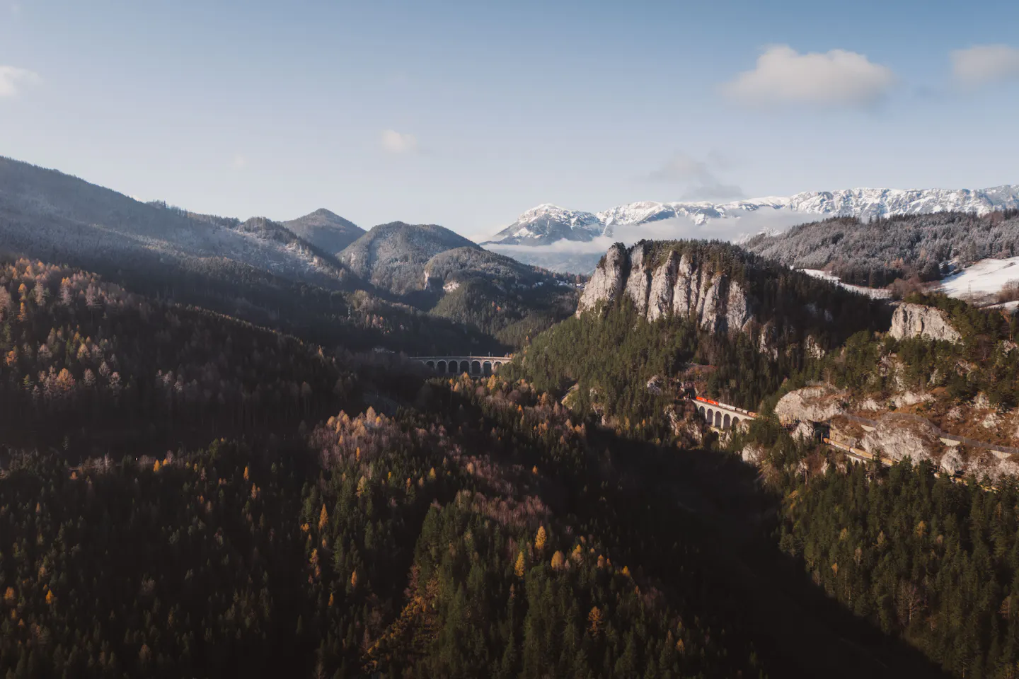 The stone arches of the Semmering railway curving round a limestone crag above autumn forest