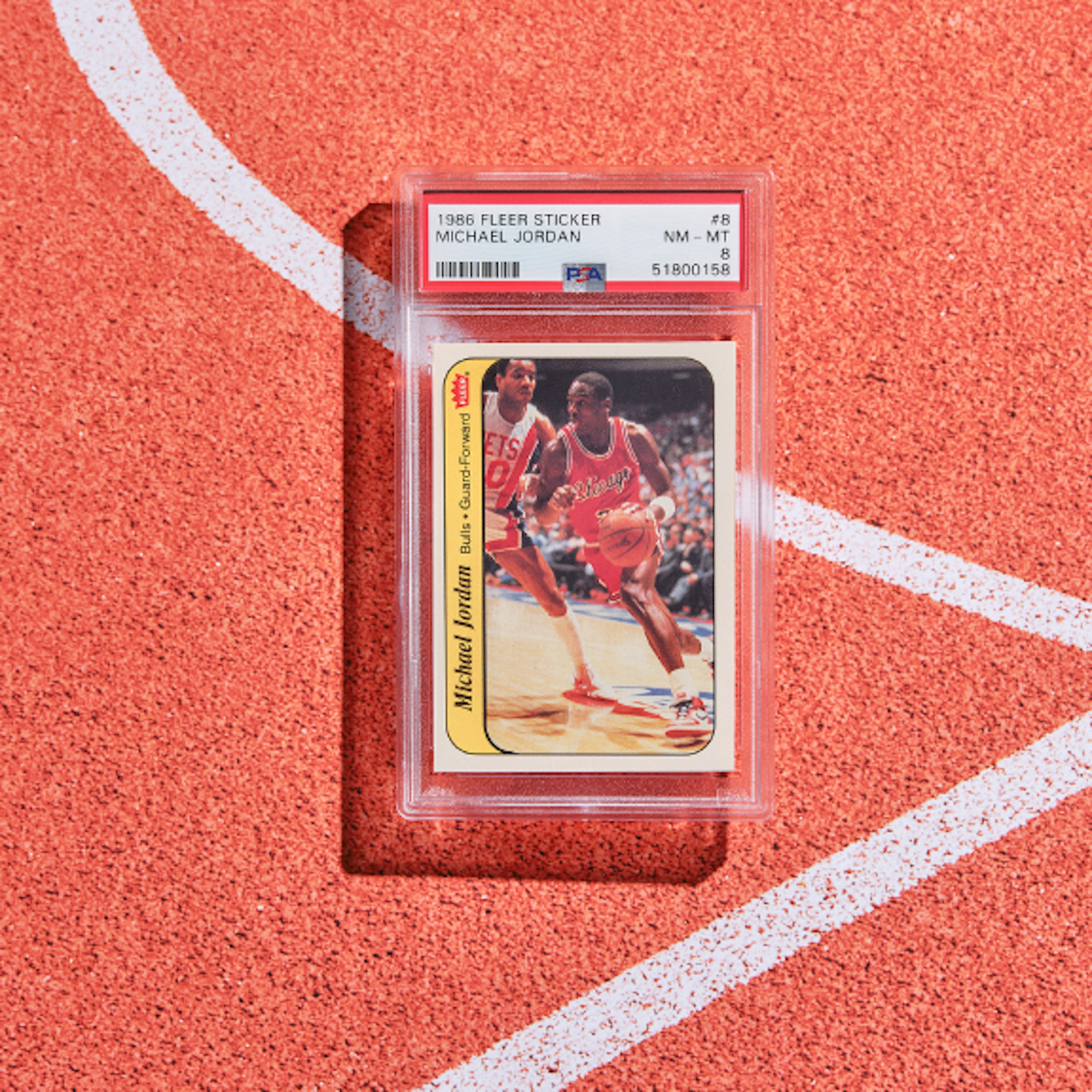A professionally graded Michael Jordan basketball trading card displayed in a protective plastic case on the surface of a basketball court.