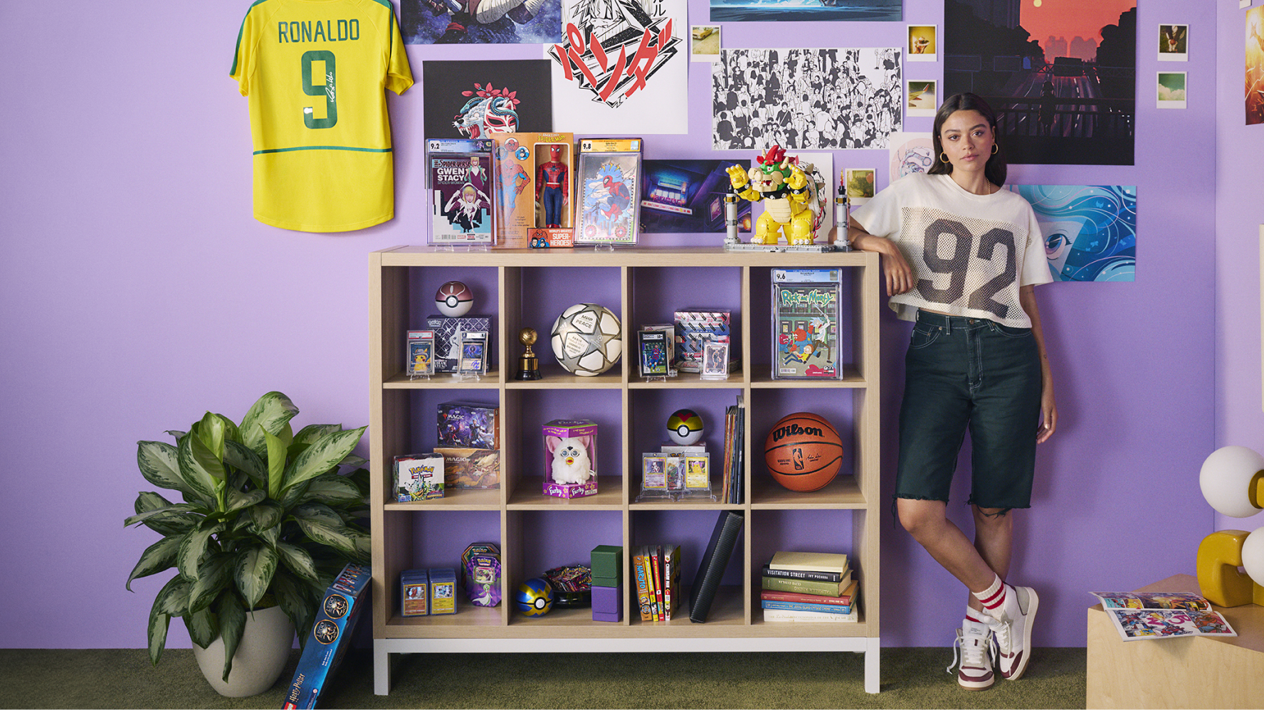 A female collector stands beside a shelving unit filled with trading cards, comics, sports memorabilia, and collectible figures, with colorful artwork and a soccer jersey displayed on the wall behind them.