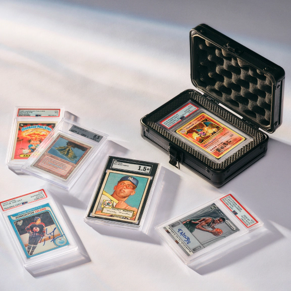 A collection of professionally graded sports and trading cards is displayed on a white surface, with one card secured inside an open protective hard case.