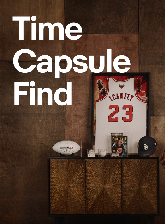 A promotional graphic featuring the headline "Time Capsule Find" above a curated display of sports memorabilia, including a framed basketball jersey, football, baseball cap, magazine, and collectibles arranged on a modern cabinet against a wood-paneled wall.