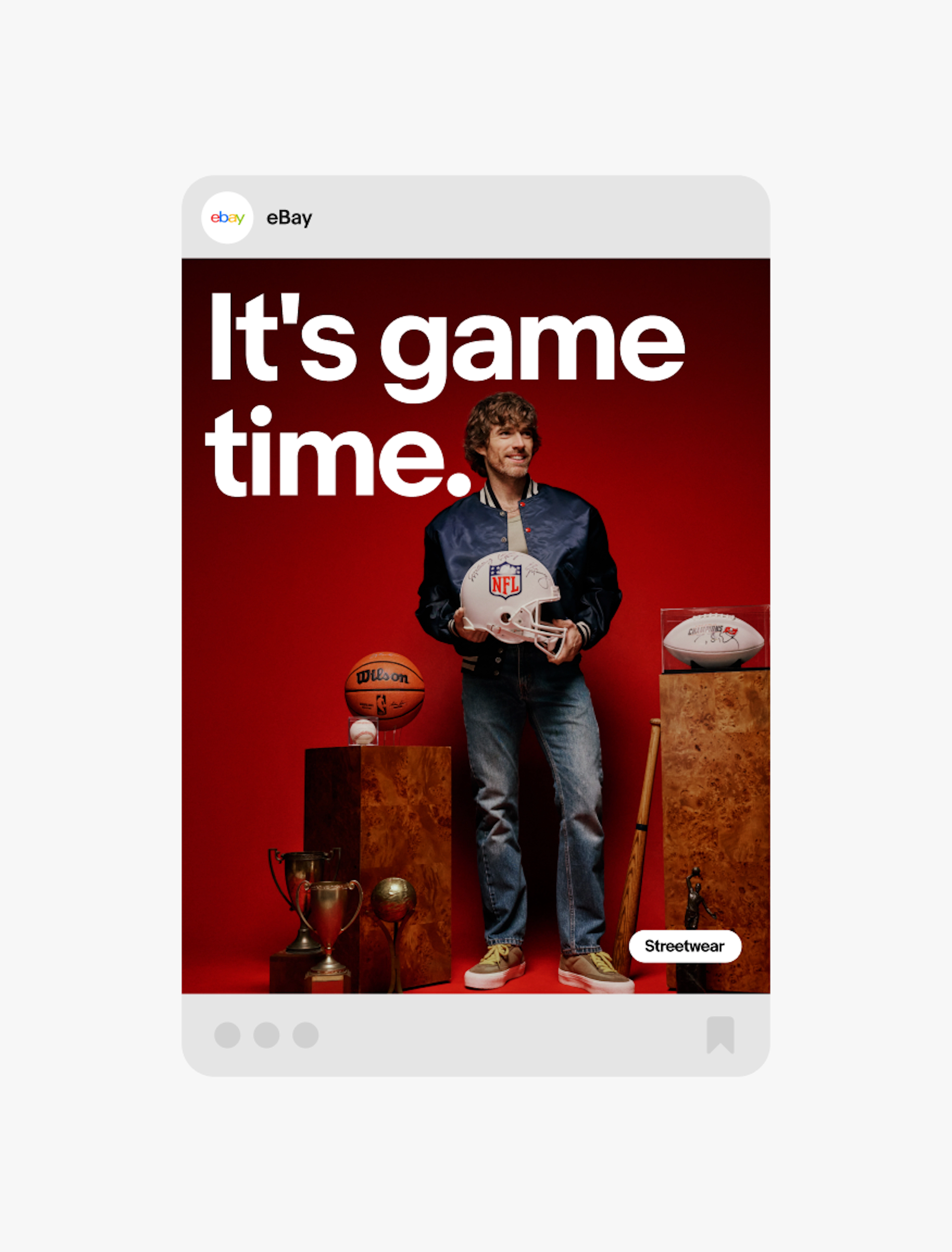 A social media-style promotional graphic featuring the headline "It's game time." above a person holding a football helmet, surrounded by sports memorabilia including a basketball, trophies, a signed football, and a baseball bat against a red background.