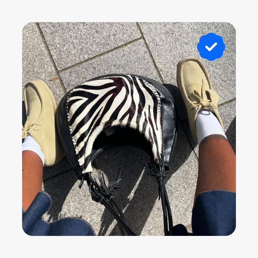 An overhead image of a person’s shoes and zebra print handbag. A blue filled Authenticity Guarantee icon is in the upper right corner.