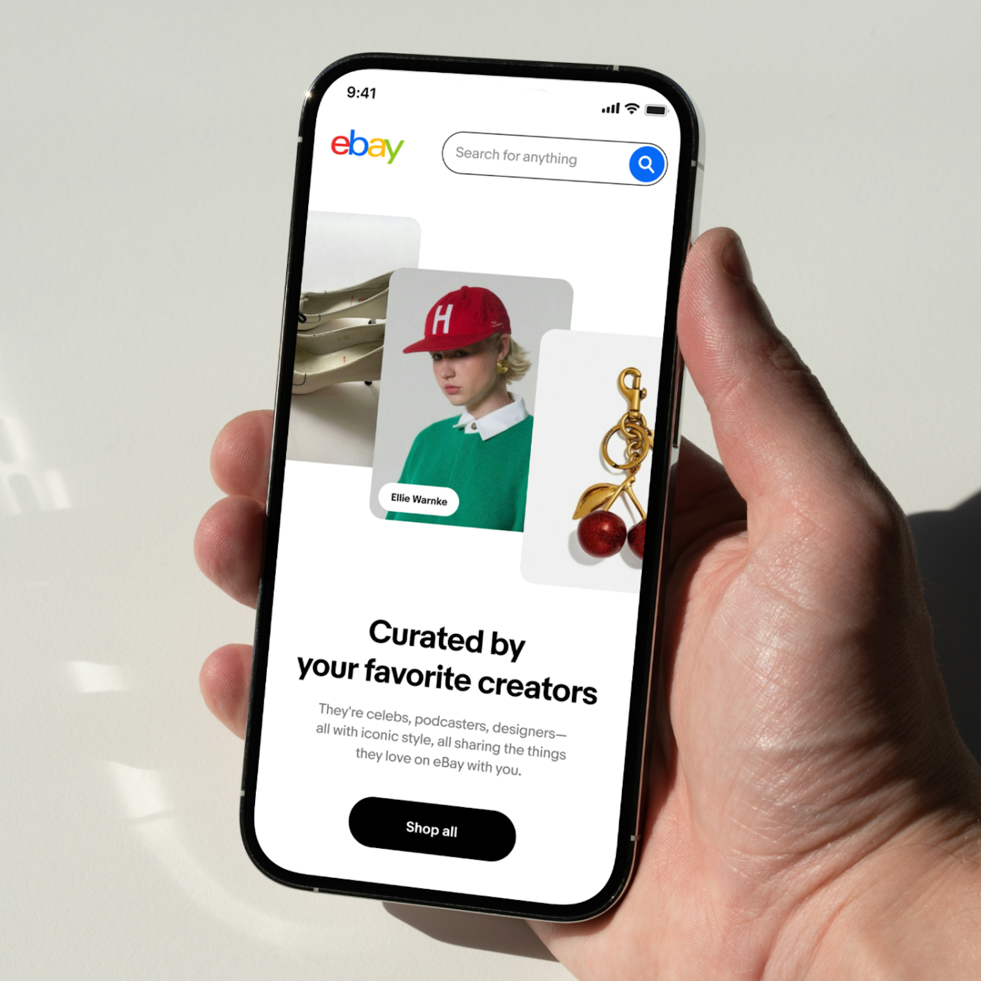 An image of the new eBay storefronts experience featuring 22 influencer-curated storefronts that are updated throughout the year. The experience is shown in a phone mockup, held by a hand resting on a white tabletop.