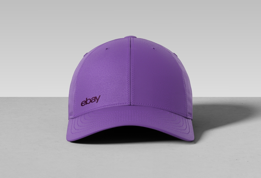 A lilac baseball hat with a tonal dark lilac eBay logo embroidered on the left side above the cap.
