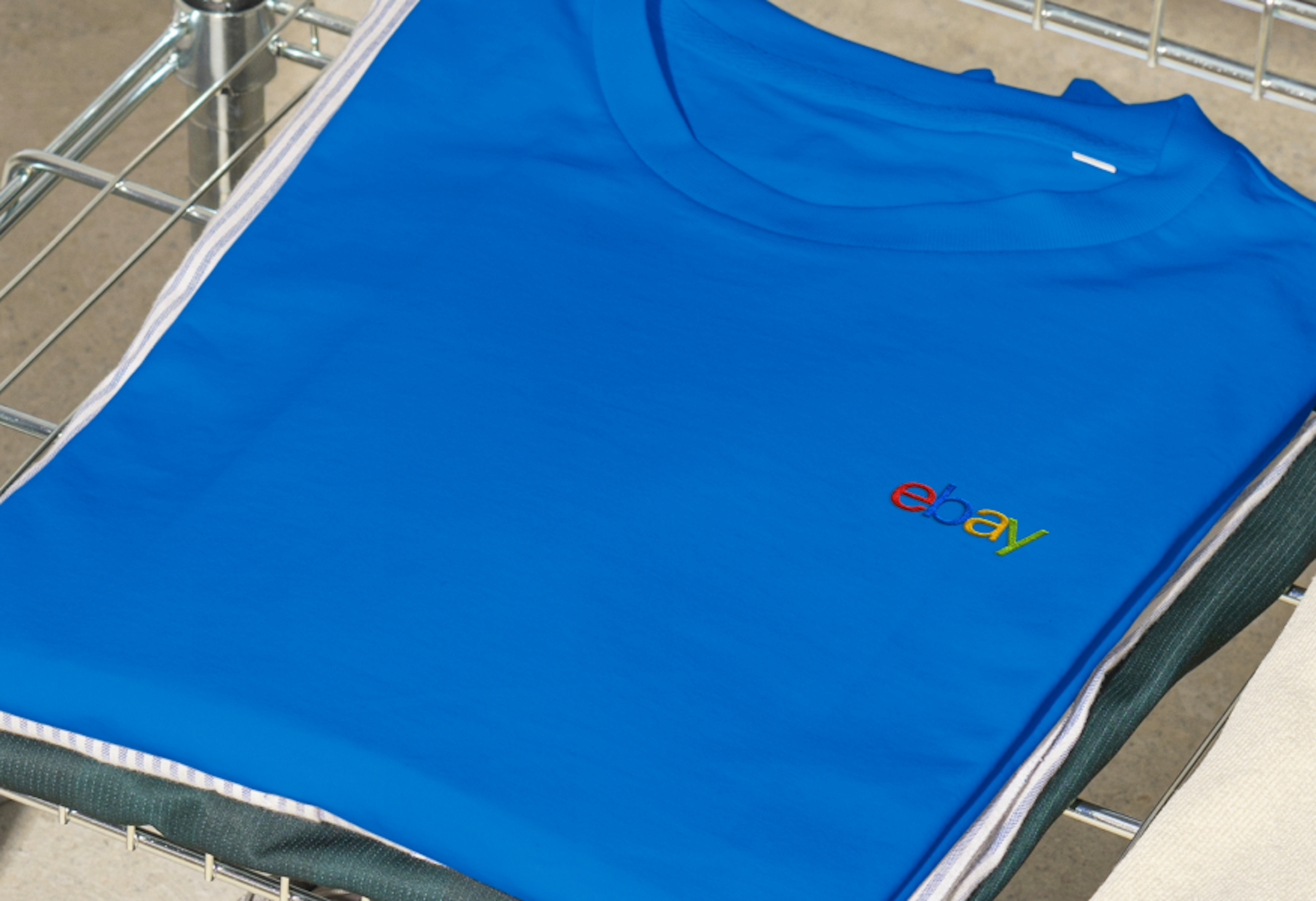 A folded blue shirt showcasing the 4-color eBay logo embroidered on the left chest area.