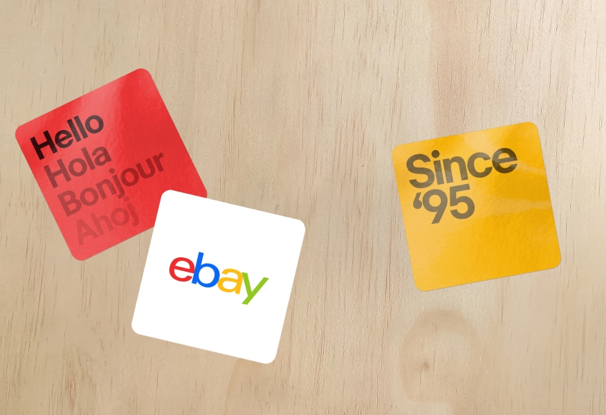A set of 3 rounded square stickers, one of which is the 4 color logo on white. The other two stickers are red and yellow, respectively, with typography and no logo.