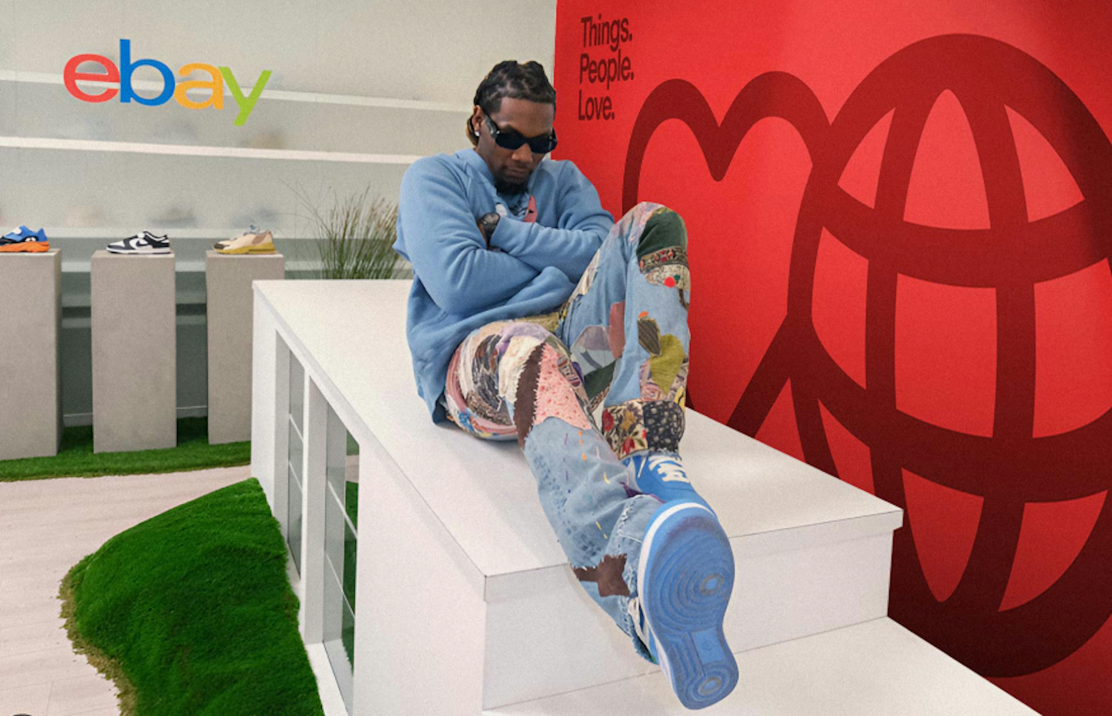 A cool looking guy in fashionable streetwear and sunglasses sitting on a white table in front of a bright red wall with the text “Things.People.Love” and a large heart and globe icon.