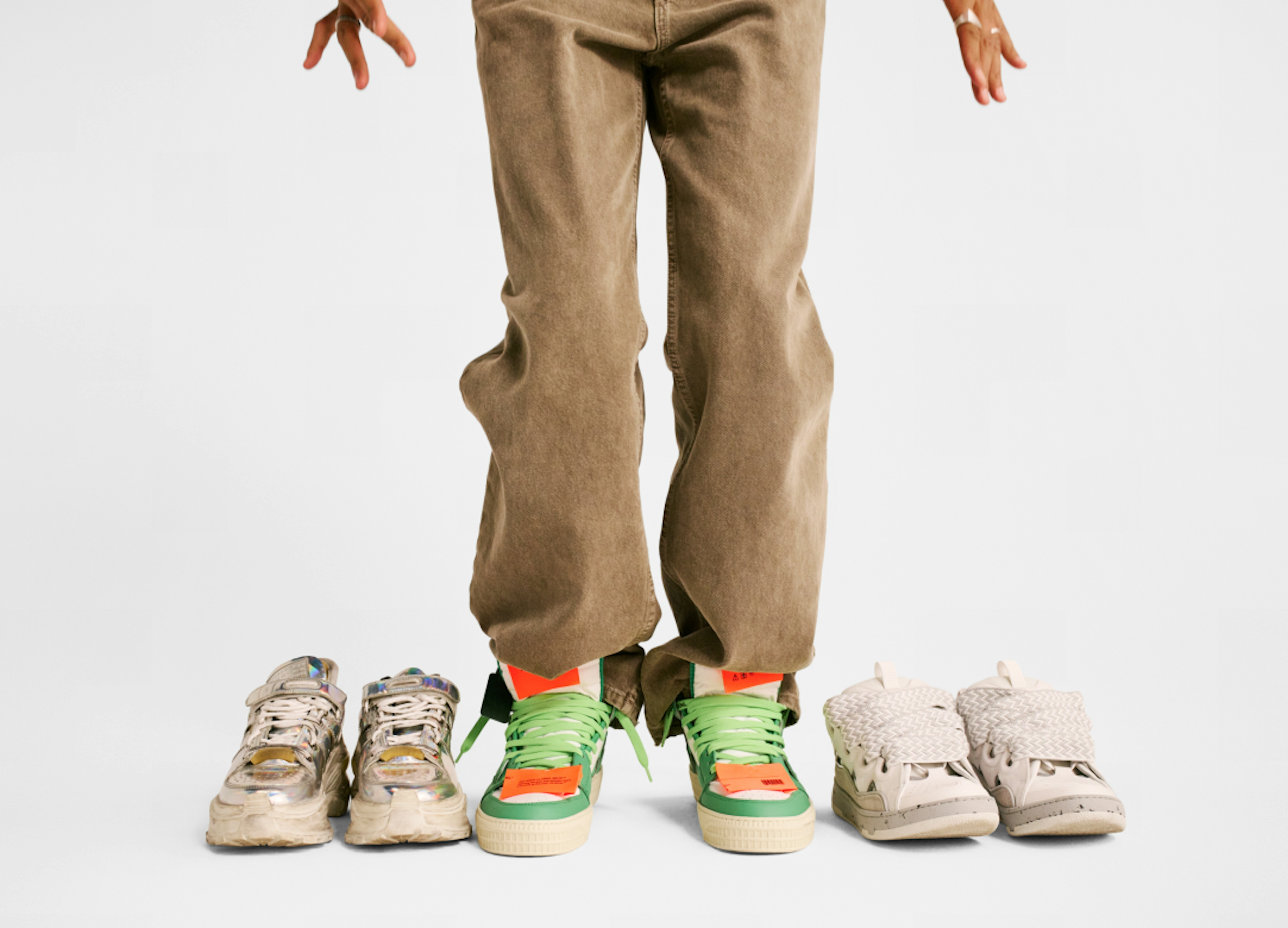Three pairs of shoes neatly arranged next to each other on the ground. Someone wearing brown jeans is wearing the pair in the center.