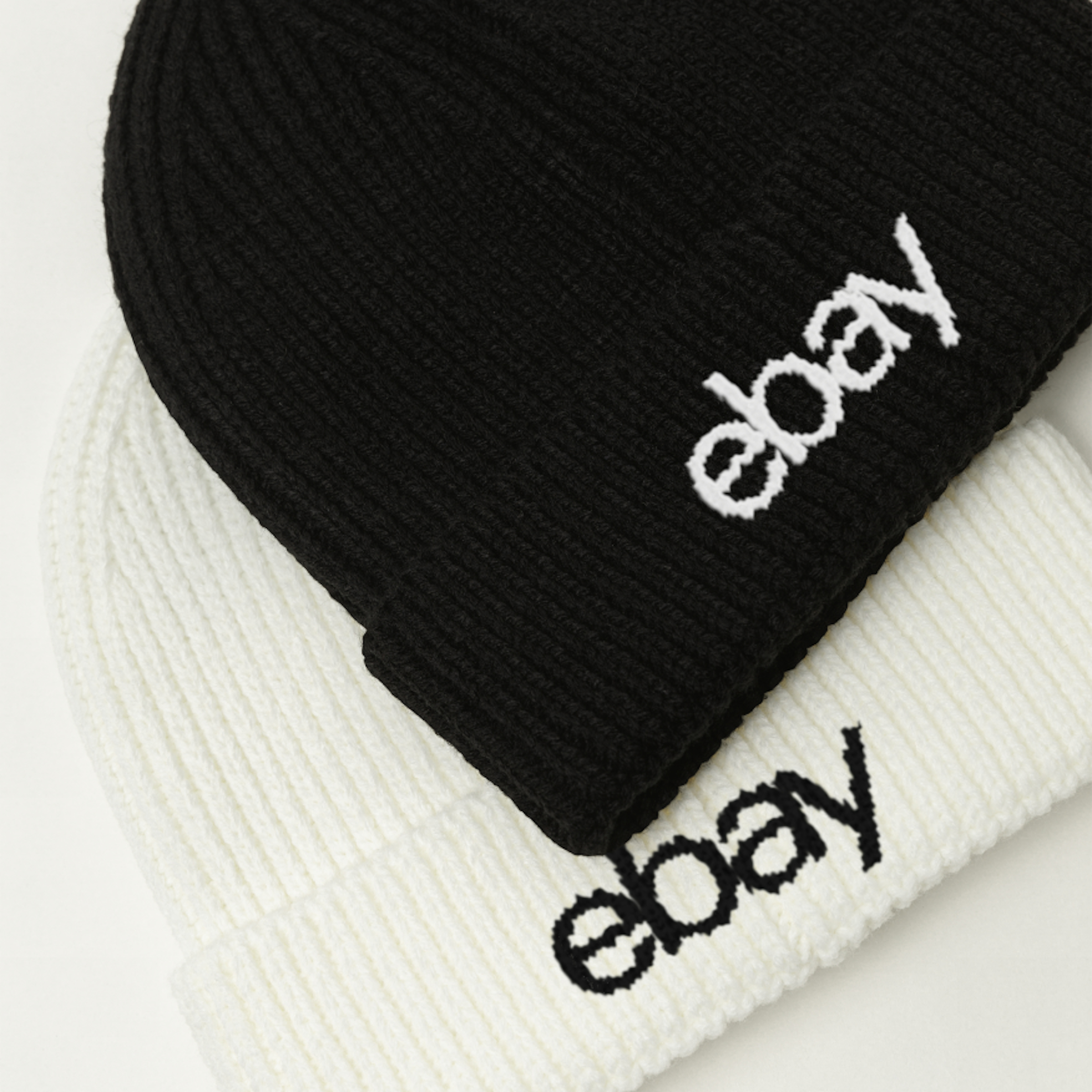 Black and white beanies with logos embroidered on them. The black beanie has a white logo, and the white beanie has a black logo.