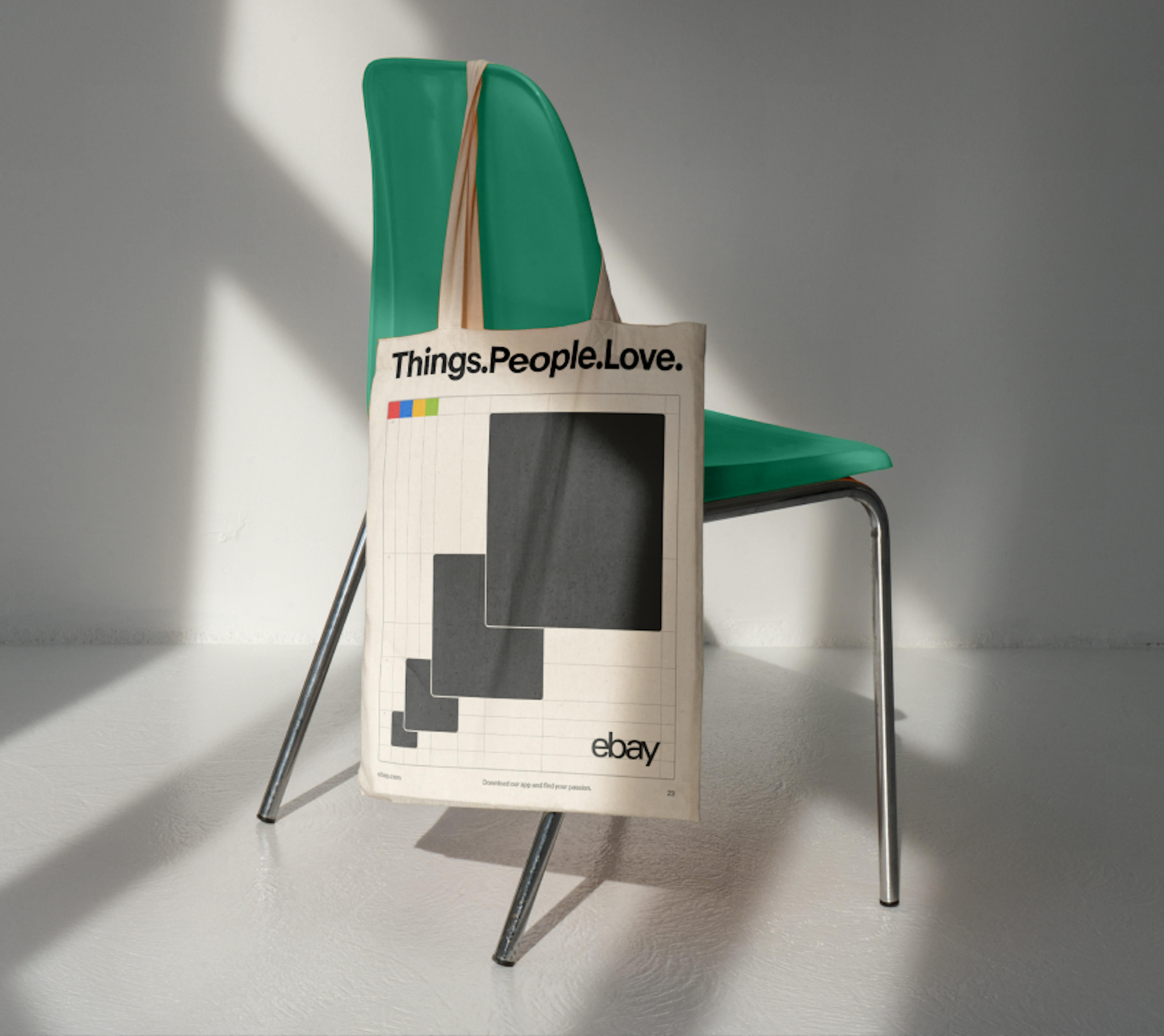 An off-white canvas tote bag with the large tagline “Things.People.Love” at the top above a graphic of growing shapes. It is hanging off the back of a modern green chair.