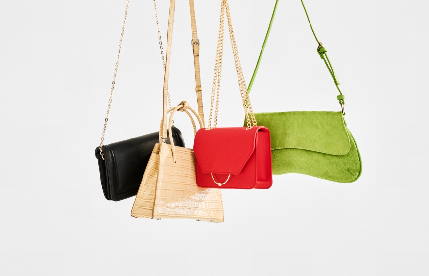 A black handbag, a tan handbag, a red handbag, and a green handbag hanging side by side against a plain white background.