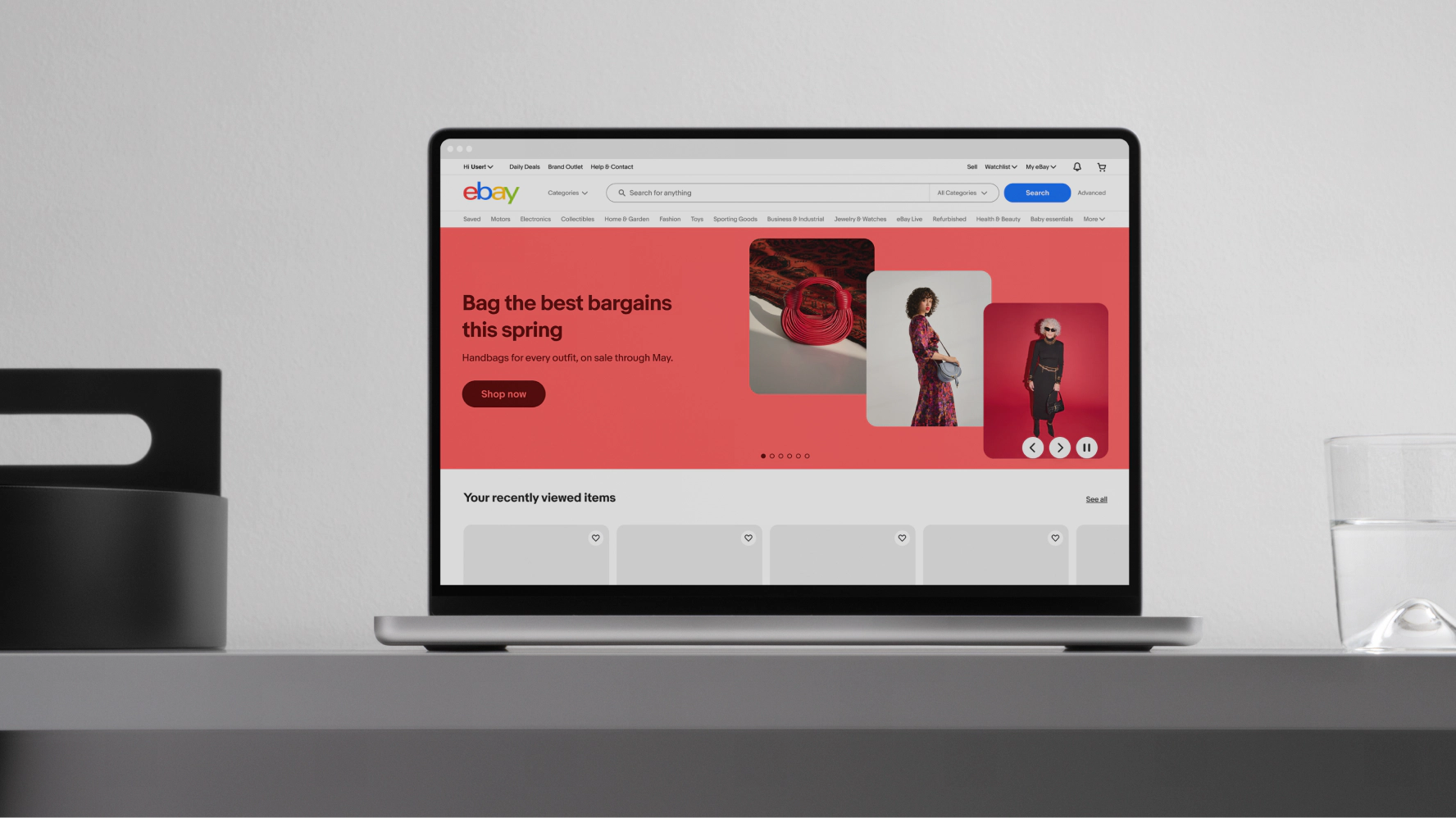 A laptop displaying the eBay website featuring a vibrant pink banner with dark pink text and button situated to the left of the banner. Three red-toned studio images complementing the banner color are stacked to the right of the banner.