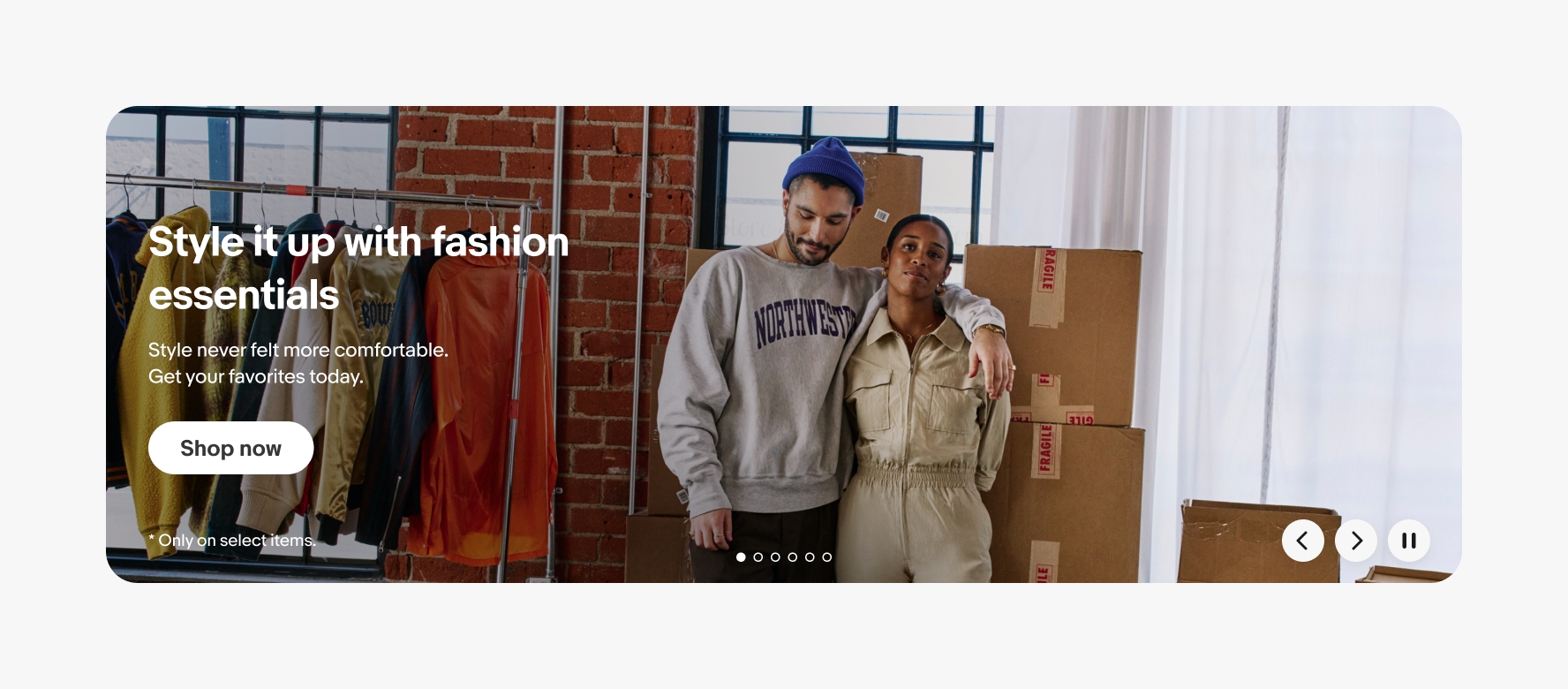 Banner with a full-bleed photo background and white text centered vertically on top. The photo is of a young man and woman business owners standing in front of jackets hanging on a rack and a stack of boxes covered in masking tape.