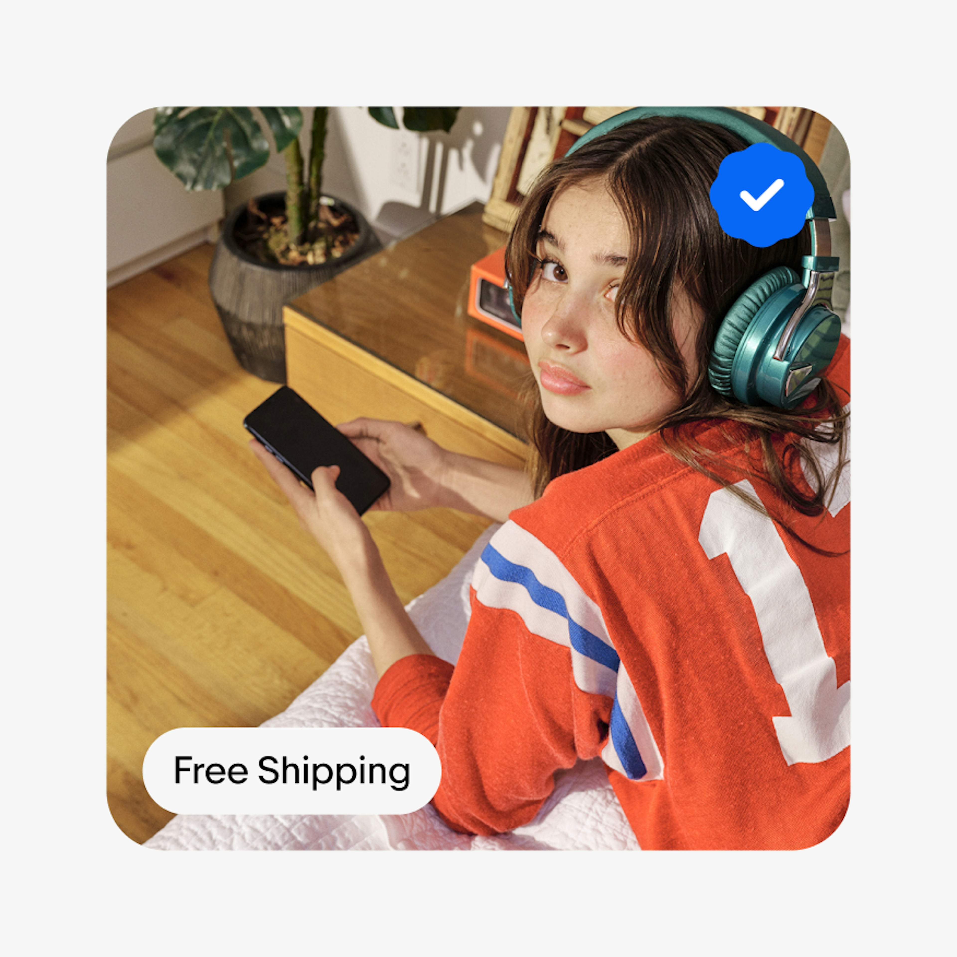 A ‘Free Shipping’ descriptive UI Element sits on the bottom left corner of a card containing a person laying on a bed facing the camera wearing headphones and holding a smartphone. An Authenticity Guarantee blue filled program badge sits on the top right of the card.