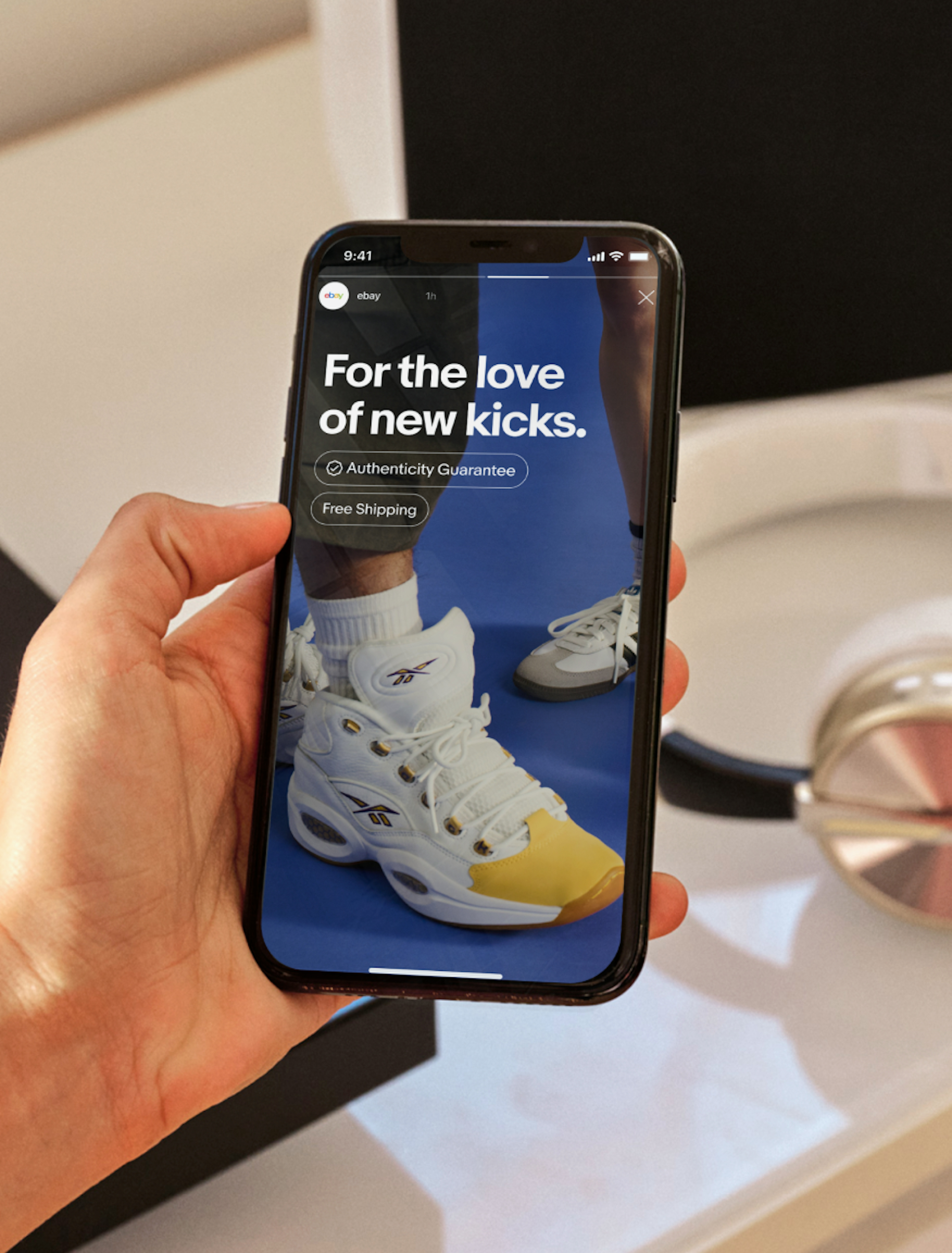 A social story is featured on a smartphone featuring two UI Elements: an ‘Authenticity Guarantee’ UI Element with an Authenticity Guarantee program badge, and a ‘Free Shipping’ descriptive UI Element, both in white. 