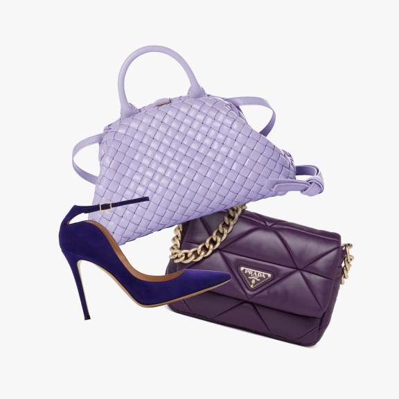 A purple high-heeled shoe, a lavender woven handbag, and a dark purple Prada handbag with a gold chain strap, displayed together as if suspended in air.