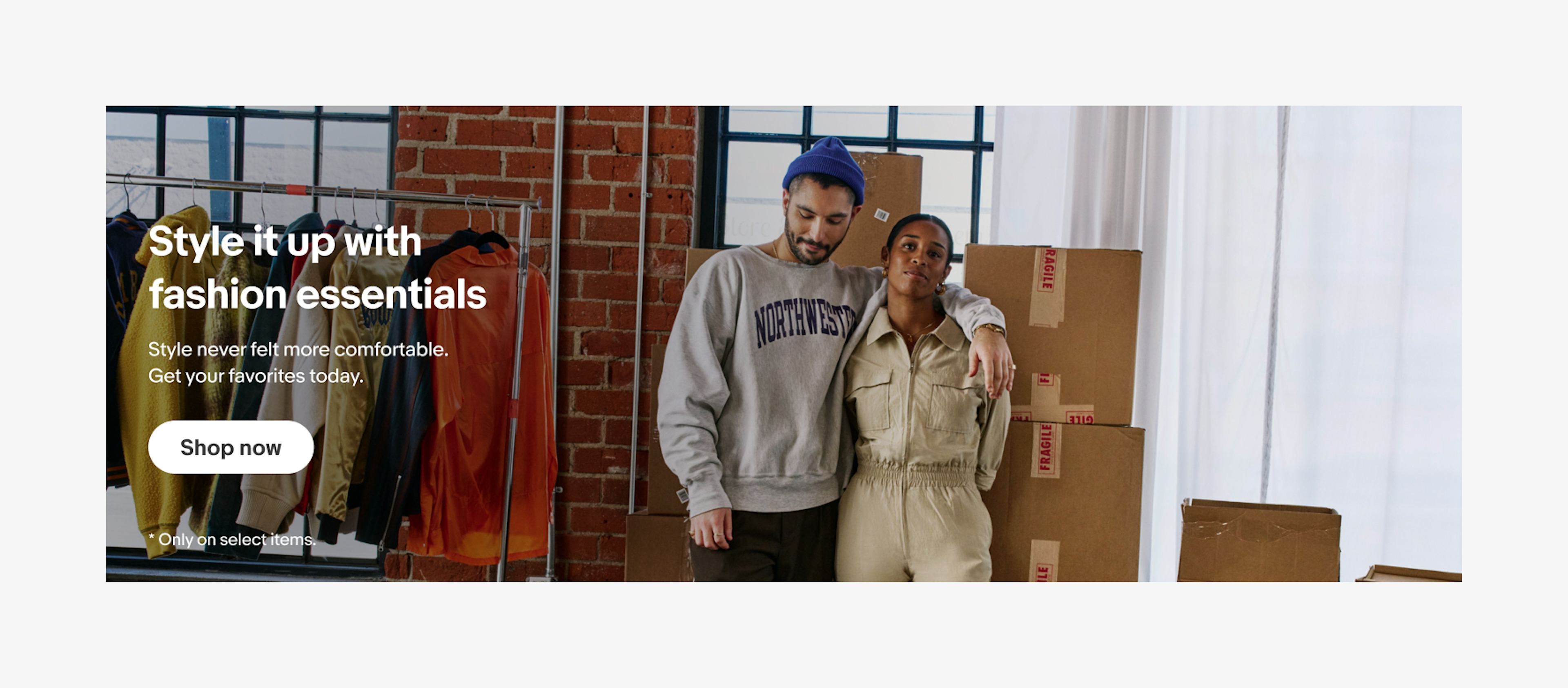 Banner with a full-bleed photo background and white text centered vertically on top. The photo is of a young man and woman business owners standing in front of jackets hanging on a rack and a stack of boxes covered in masking tape.