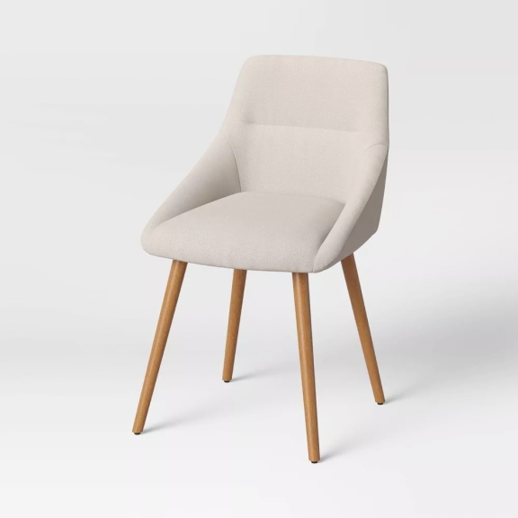 The image features a modern a beige fabric dining chair with a minimalist design against a white seamless backdrop.