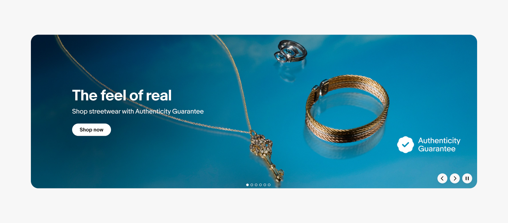 A large product banner with text on the left side containing a headline, subline, and cta button. The image contains a vibrant blue background with 3 types of jewelry. The program badge is randomly placed on the right side of the banner.