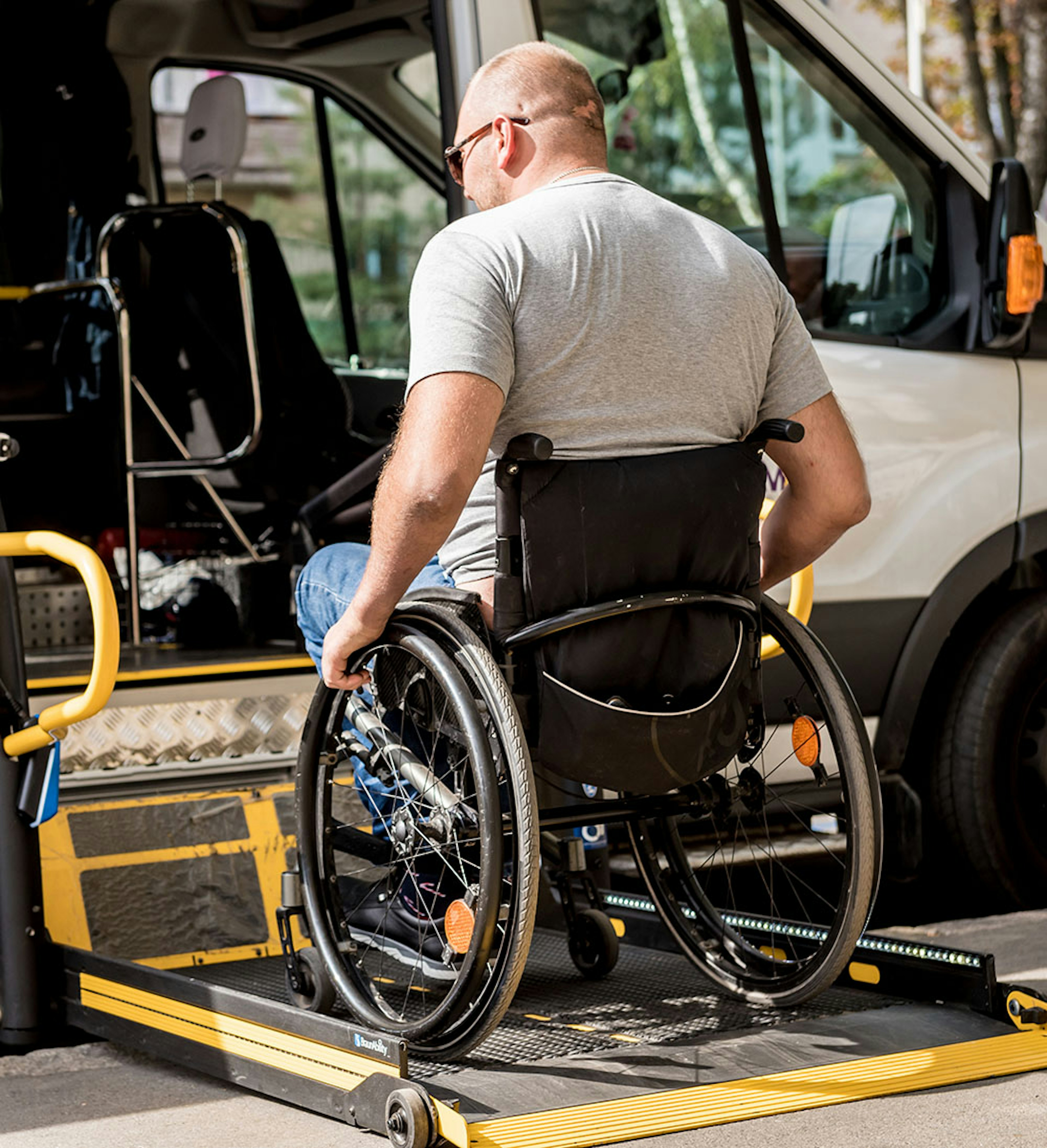Wheelchair user boarding an accessible transit van using a deployed platform lift at the curb.