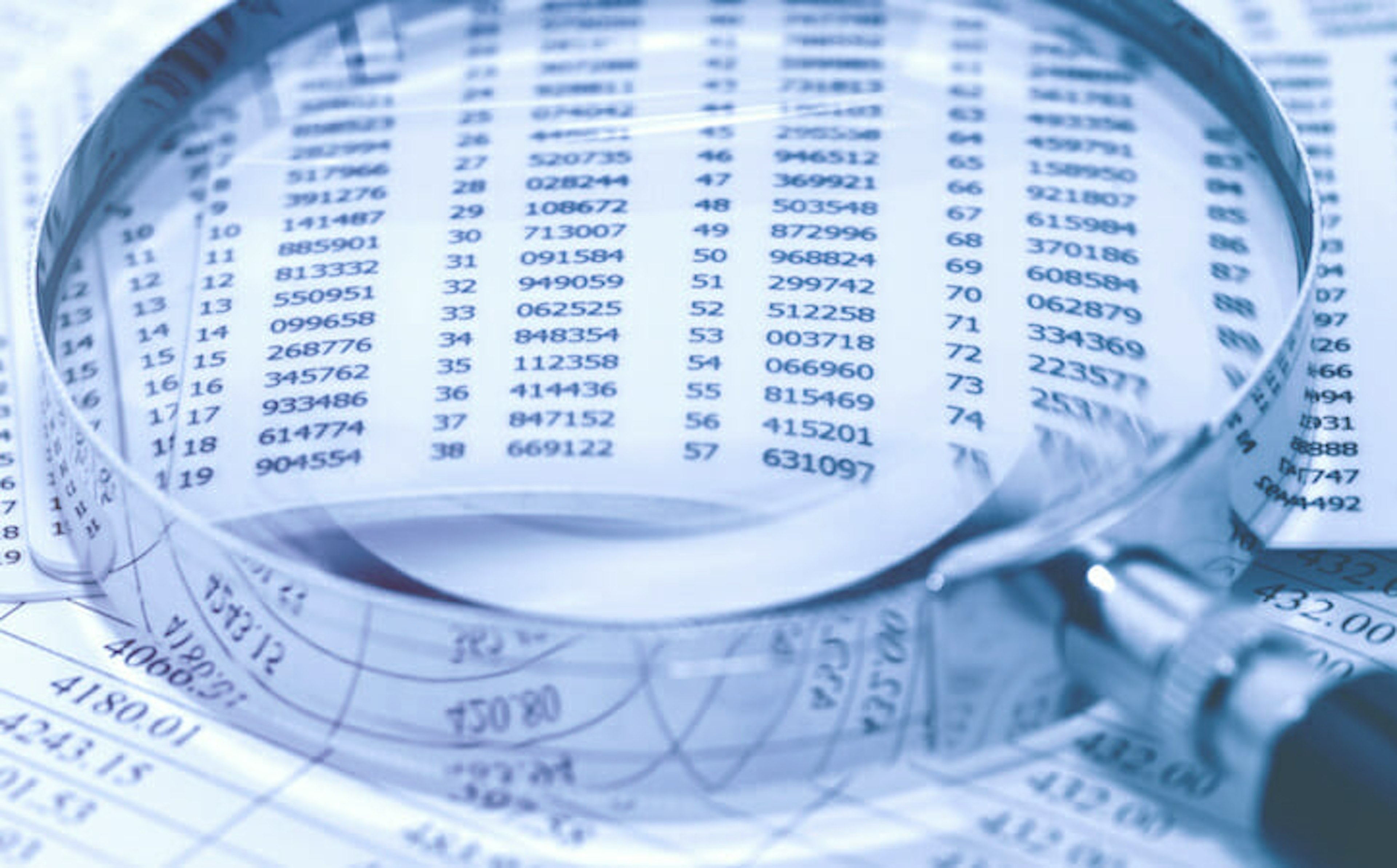 Magnifying glass resting on a spreadsheet filled with numbers, symbolizing data review or auditing.