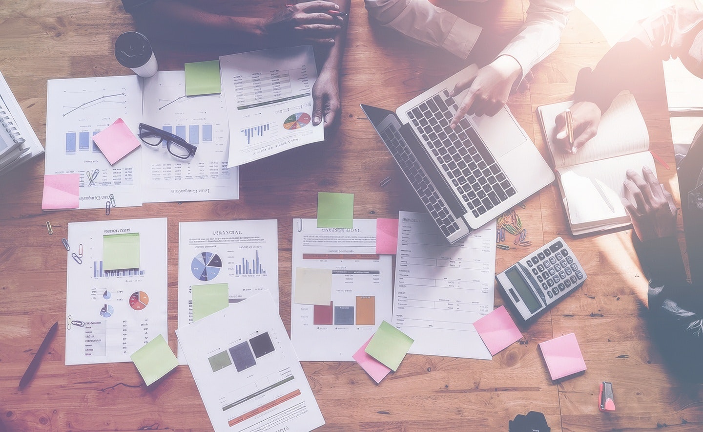 Overhead view of a team collaborating around a table with charts, reports, sticky notes, and laptops.