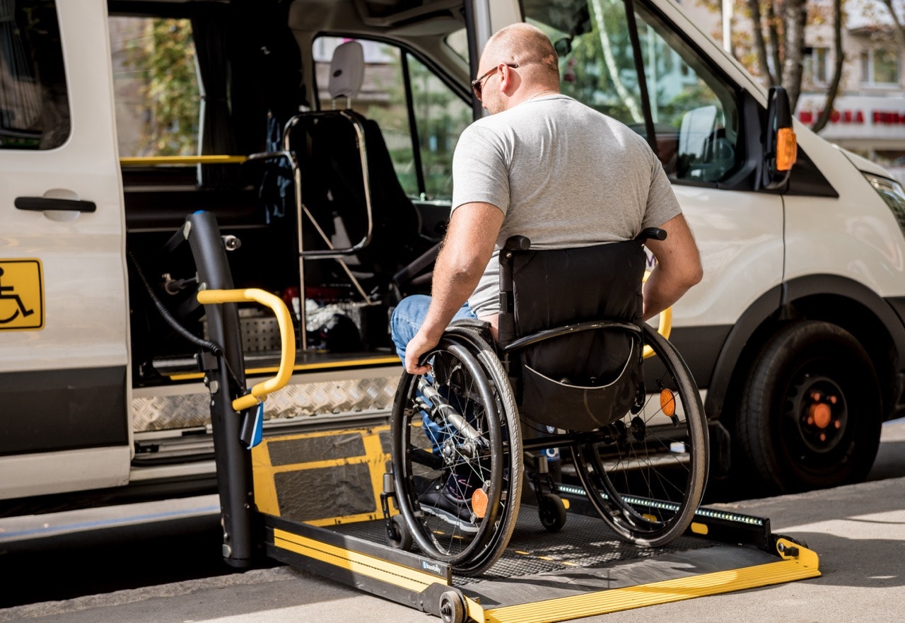 Wheelchair user positioned on a lowered platform lift entering an accessible transit van parked at the curb.